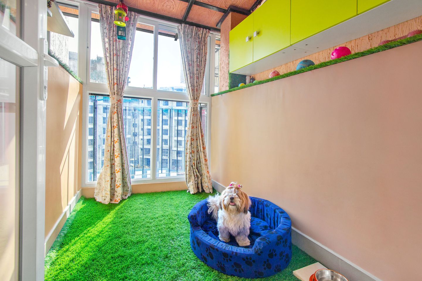 Modern Balcony Design with Light Pink Accent Wall, Yellow Lofts, Closed Balcony Space, Green Grass Mat, and Curtains - Livspace