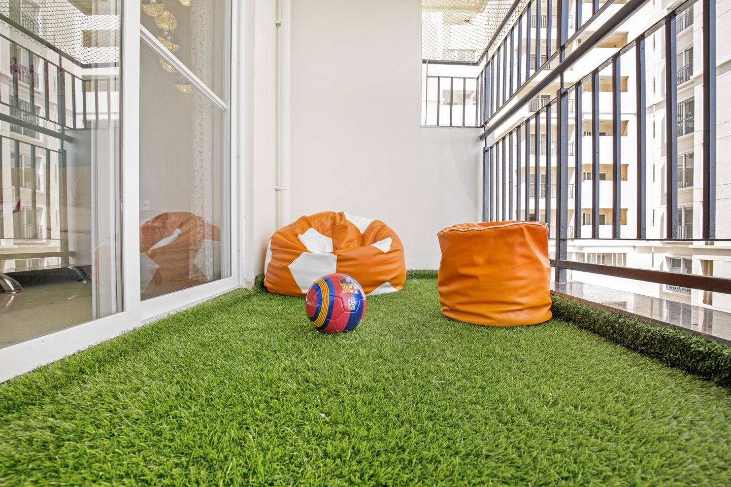 Minimal Balcony Design with Off-White Wall, Green Grass Mat, Orange Pouffe, and Beanbag - Livspace