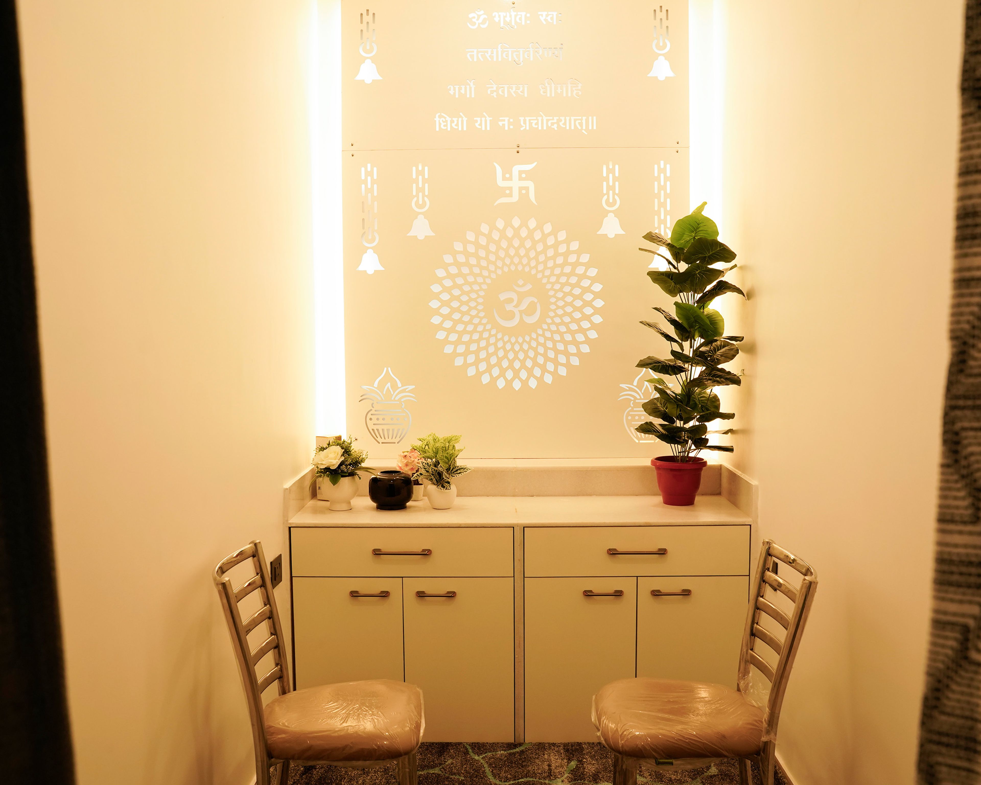 Pooja Room Design with Illuminated Background Wall with Spiritual Symbols, Cabinet and Two Chairs