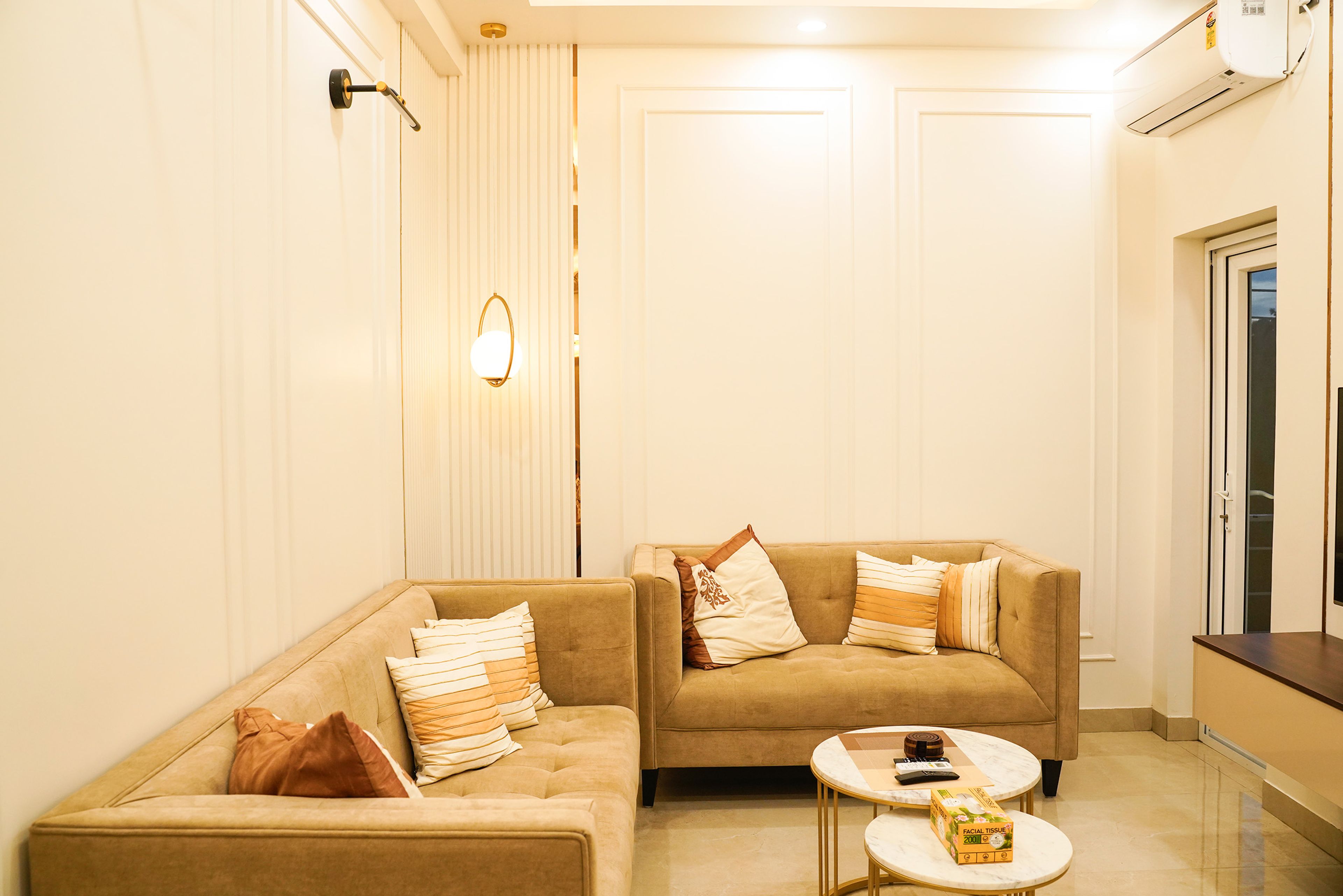 Living Room Design with Twin Beige Sofas, Gold Wall Light, and Round Marble Coffee Tables