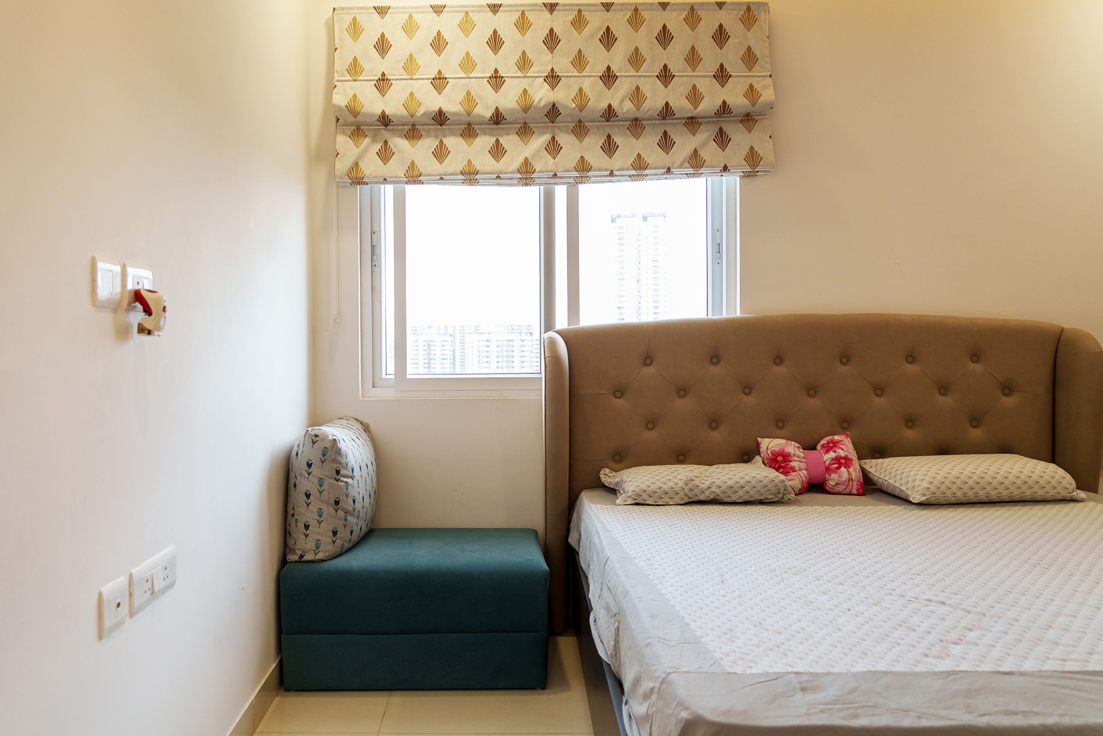 Bedroom Design with Tufted Beige Headboard, Green Window Seat, and Printed Roman Blinds