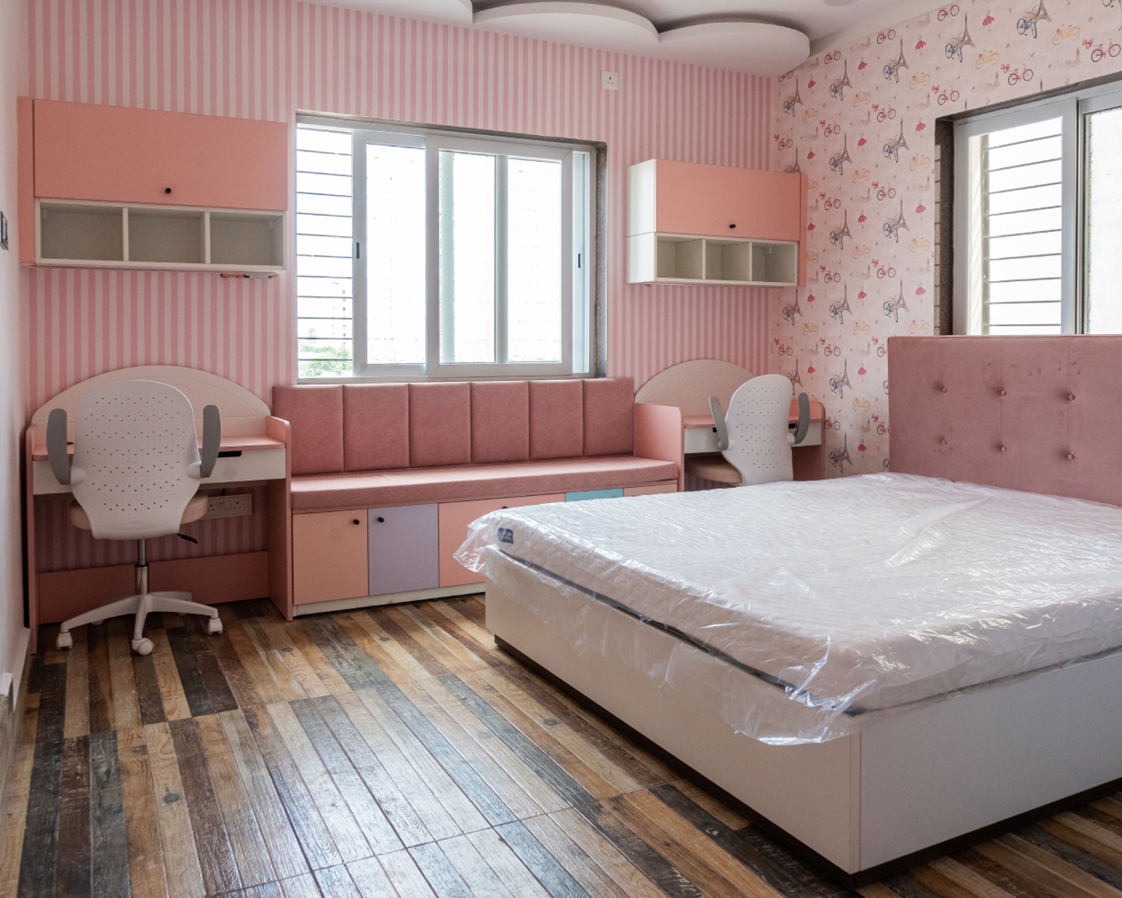 Kids Bedroom Design with Pink Cushioned Seating Bench with Storage, 2 Pink and White Study Tables and Pink and White Striped Wallpaper