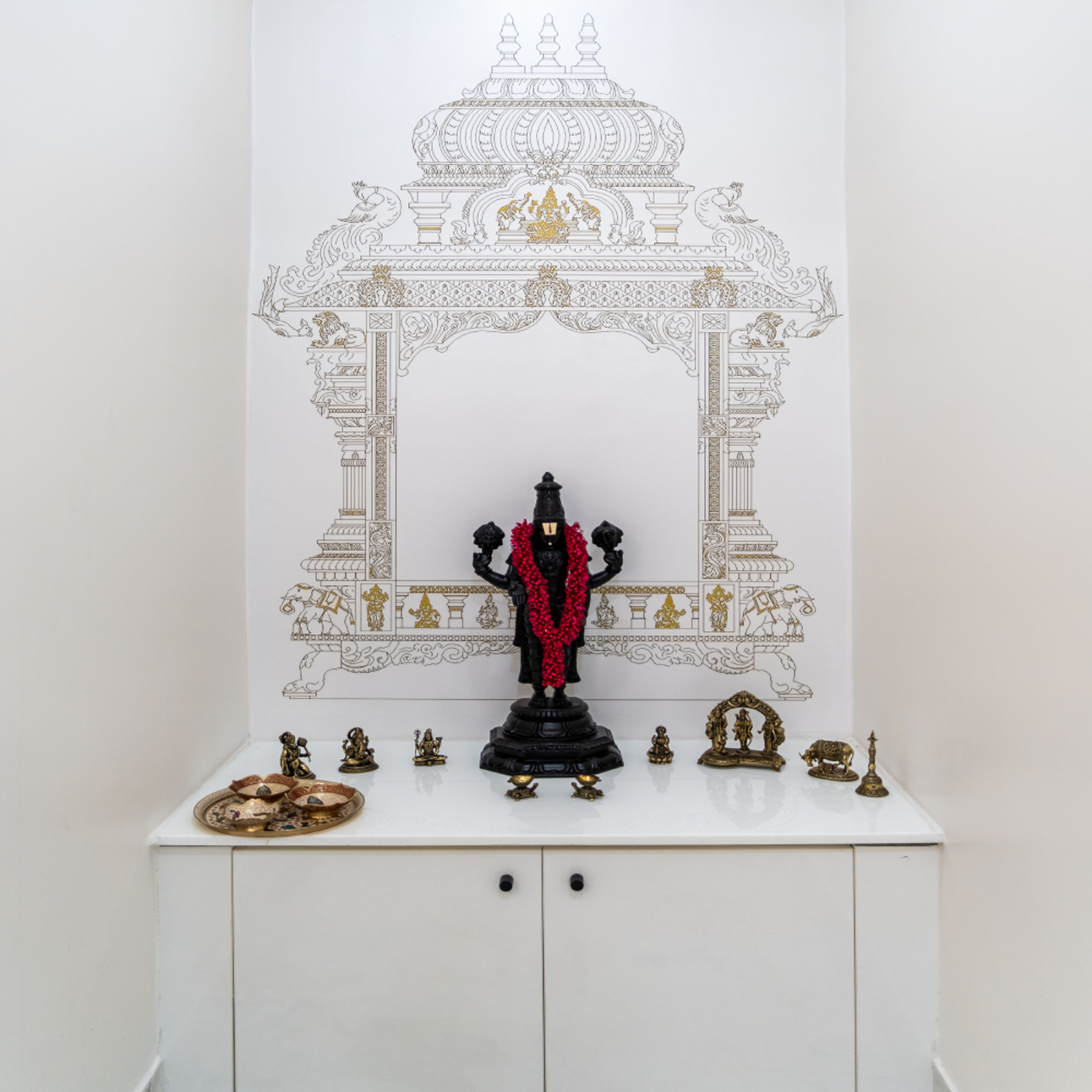 Pooja Room Design with Intricate Temple-Themed Wallpaper, White Cabinetry, and Traditional Brass Idols