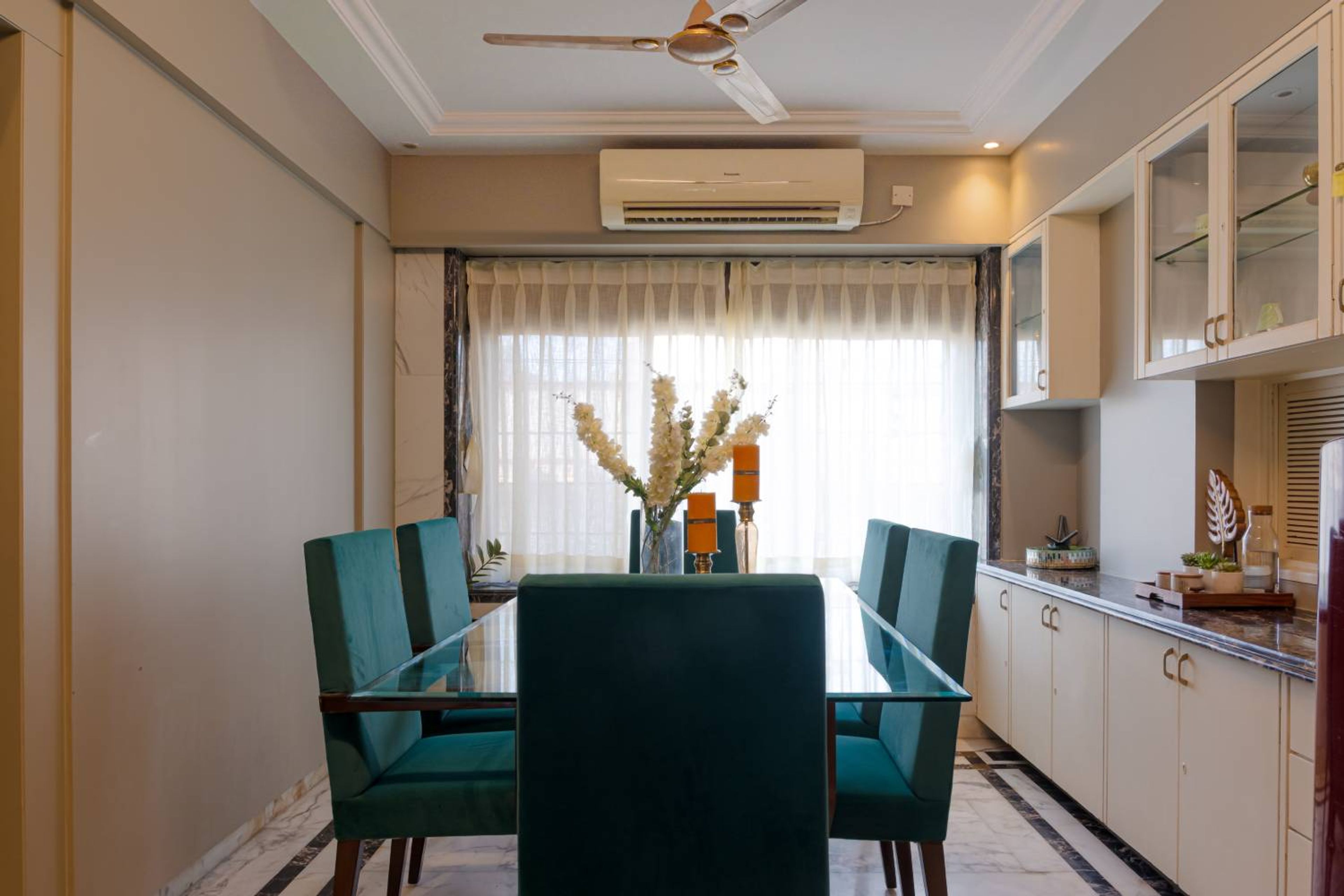 Dining Room Design with Rectangular Glass Table, Teal Upholstered Chairs and Cream Crockery Unit