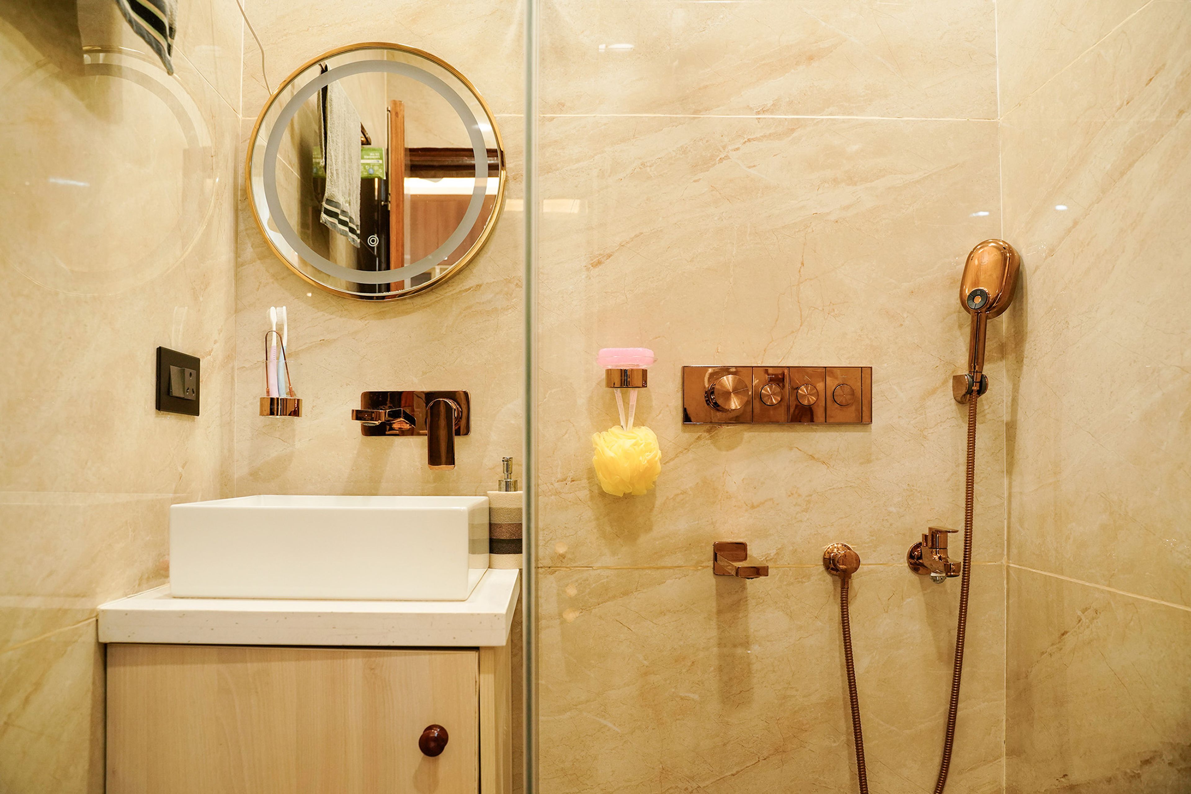 Bathroom with golden fixtures, round mirror, and glass-enclosed shower space