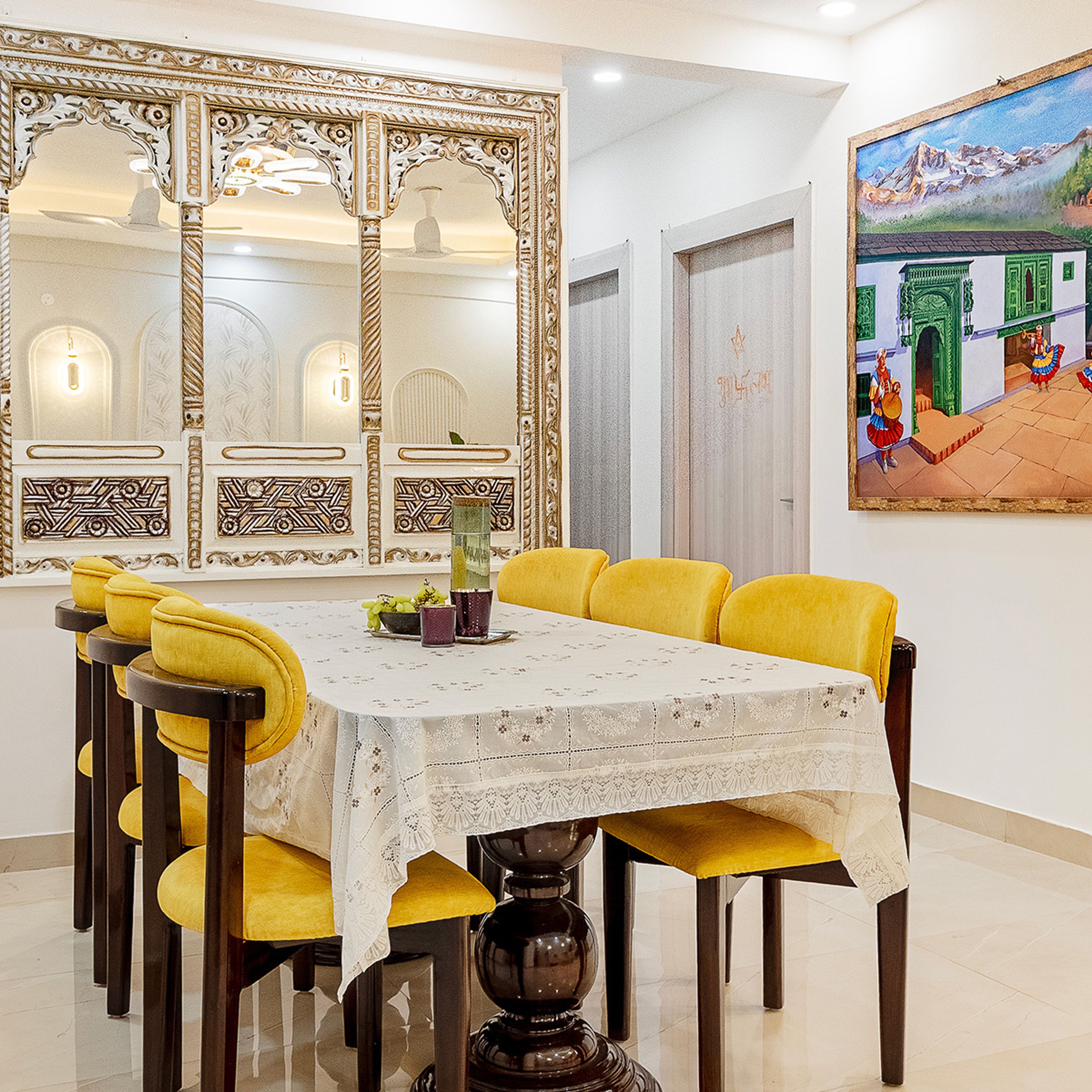 Dining room with ornate mirrors, yellow chairs, patterned tablecloth, and cultural artwork
