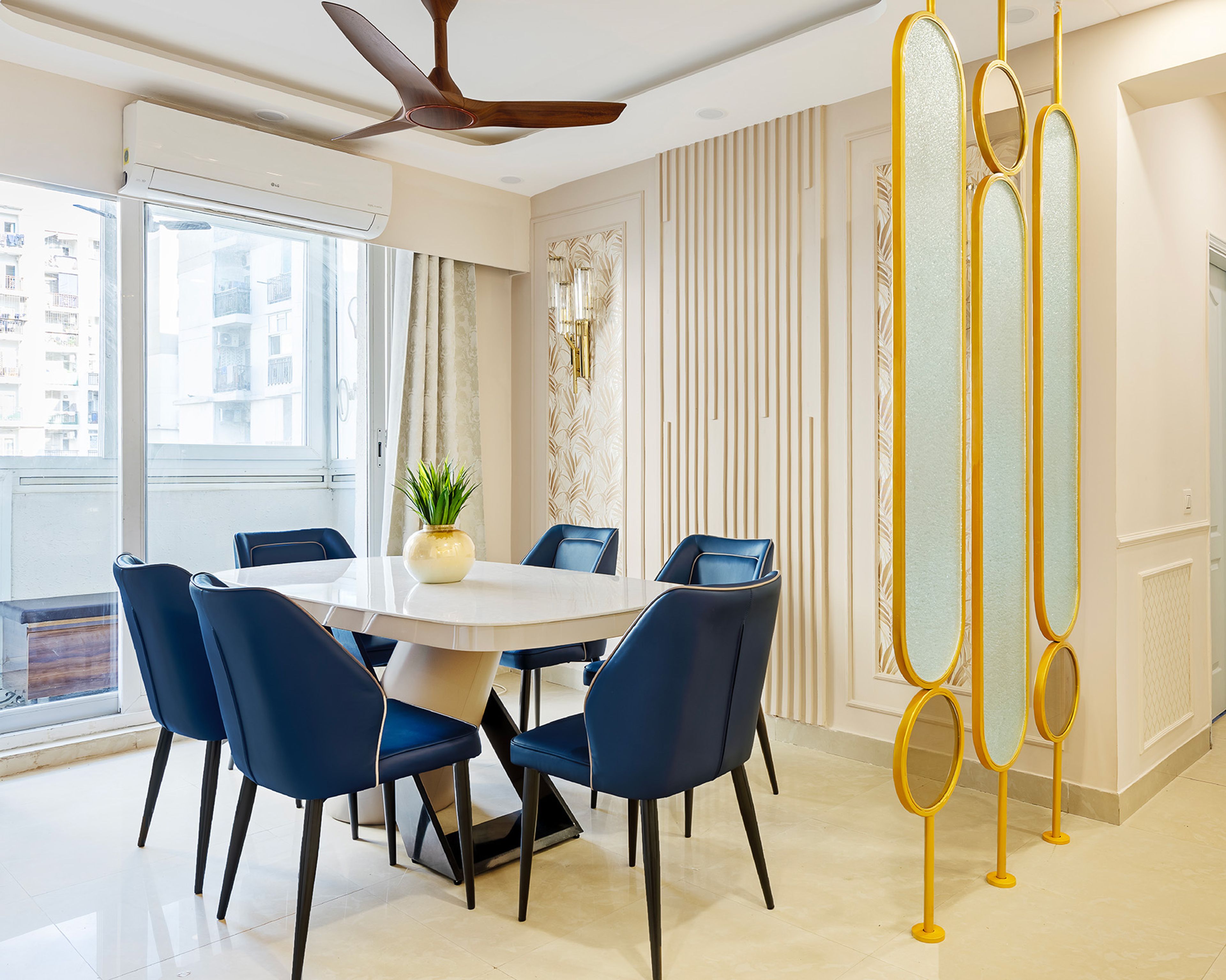 Dining room with blue chairs, white table, golden divider, and natural light