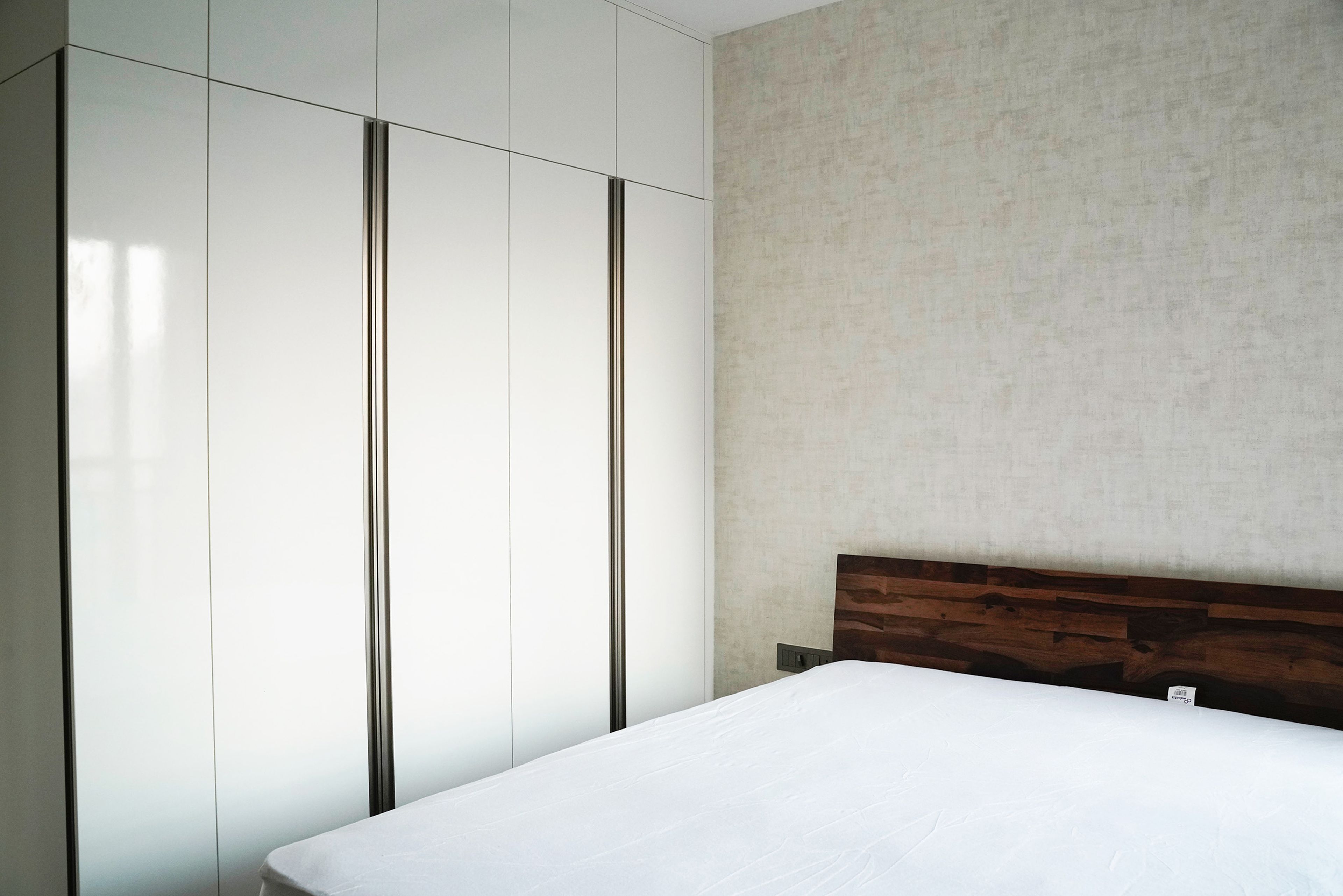 Guest bedroom with wooden bed frame, light beige walls, and balcony access