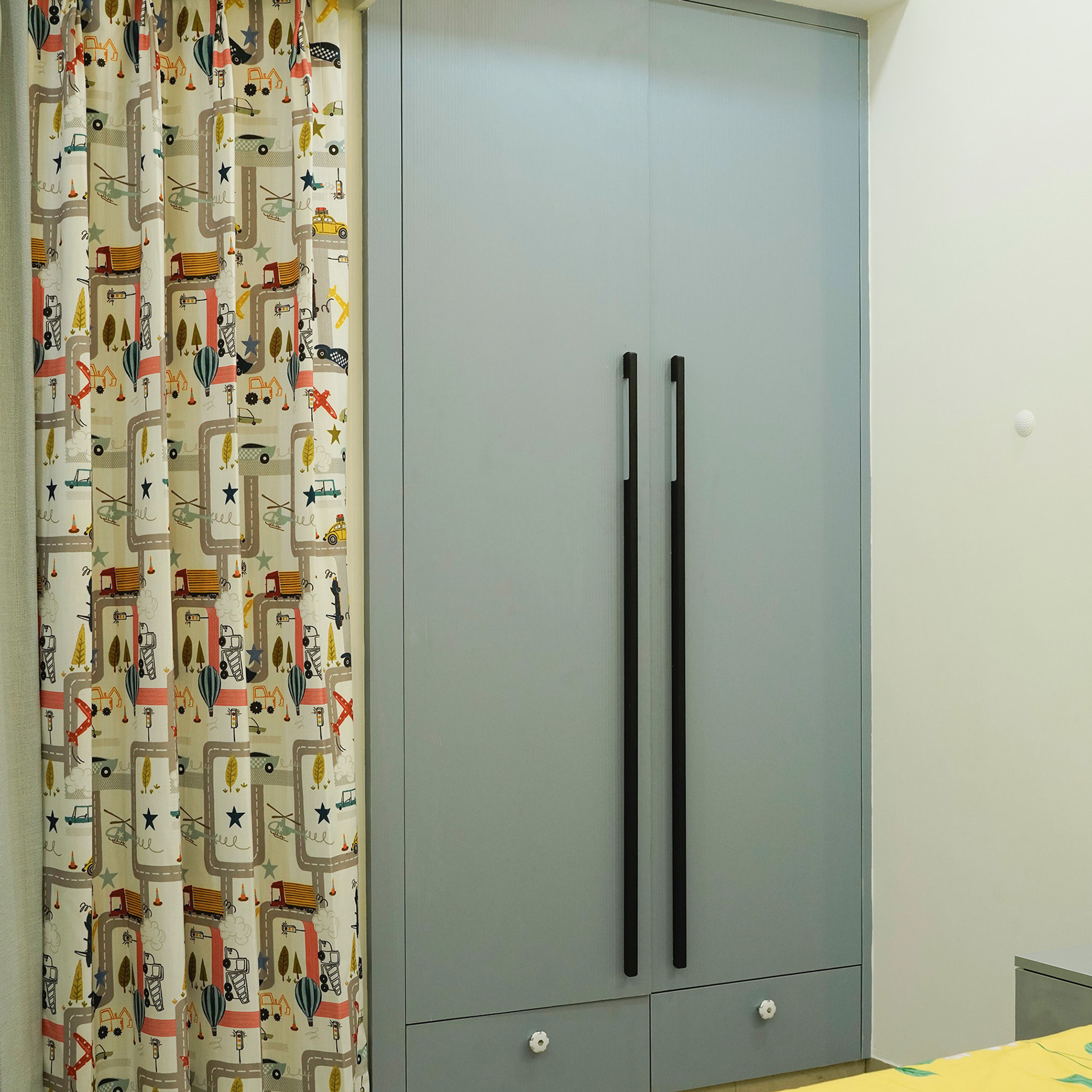 Space-themed kids’ bedroom with blue accent wall, yellow floral bedding, and sleek grey wardrobe