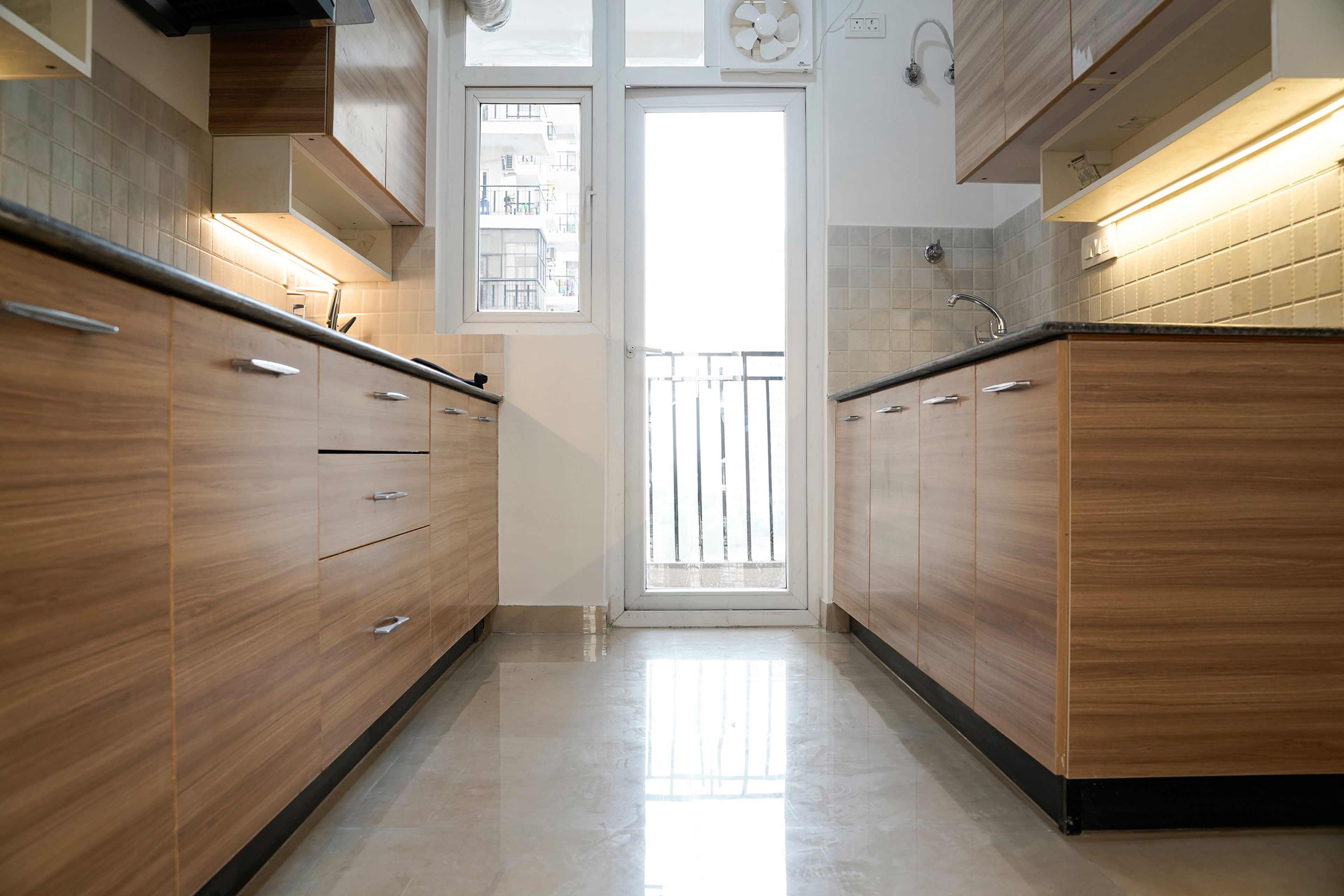 Parallel wooden kitchen with white upper cabinets, black countertop, and under-cabinet LED lighting
