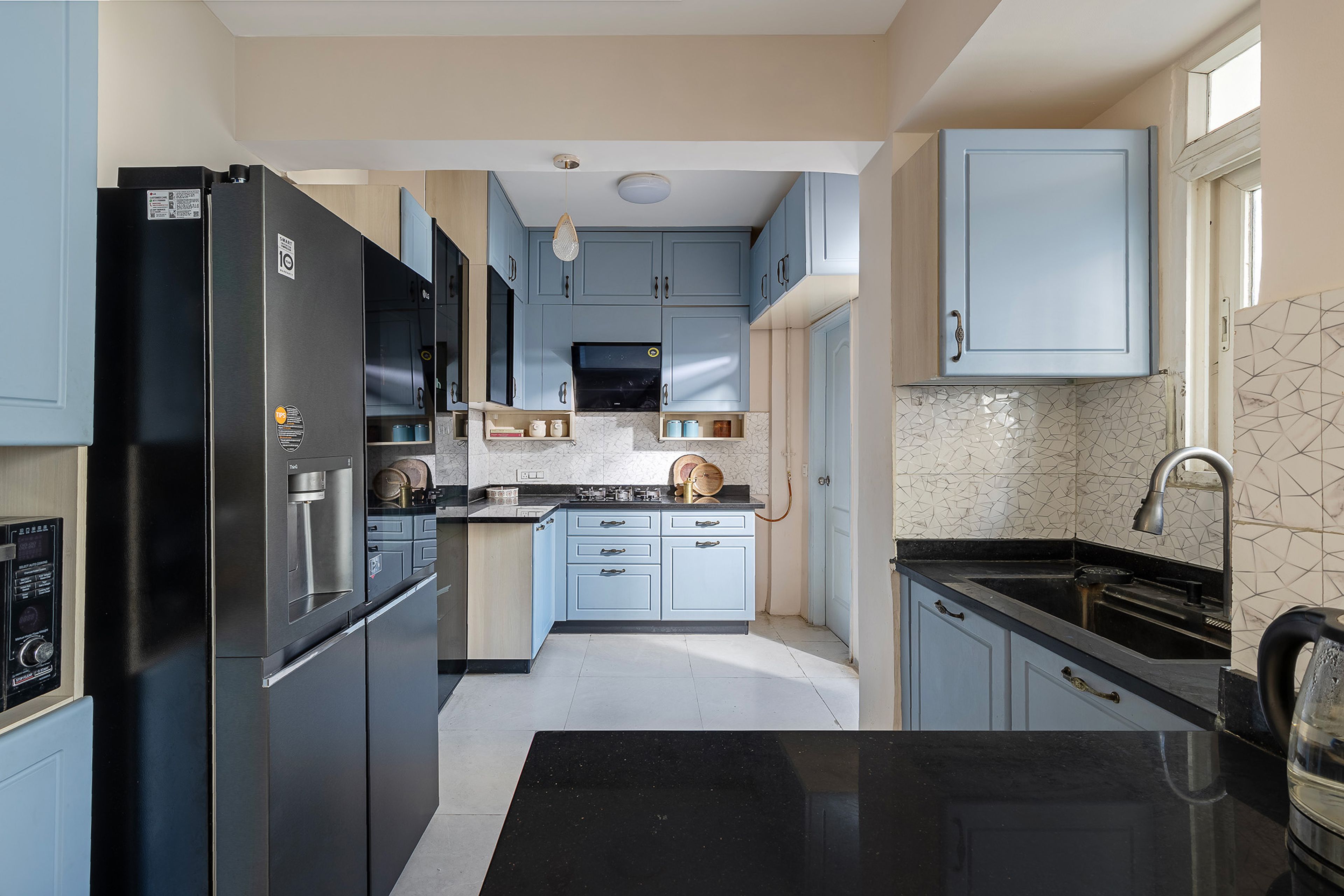 L-Shaped blue modular kitchen with glass display cabinet, black countertop, and patterned backsplash