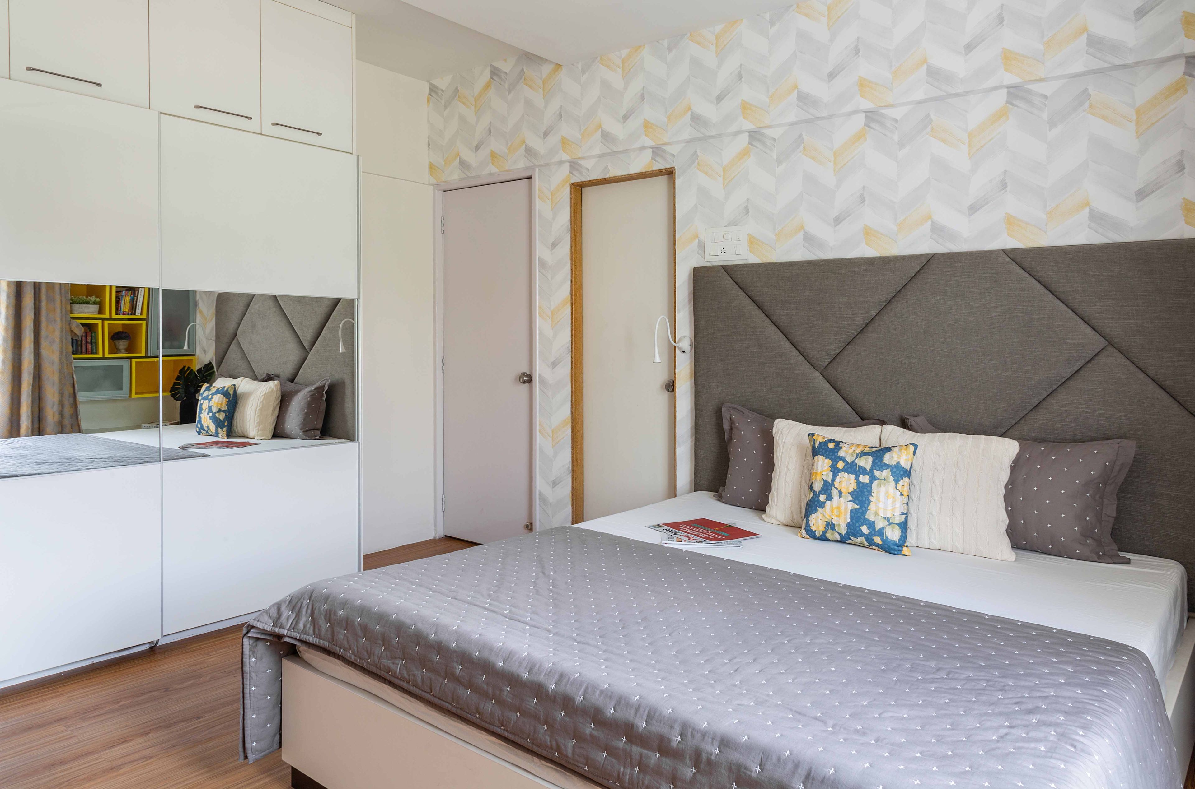 Minimalist Guest Room Design With Grey Queen Bed, Chevron Wallpaper, Mirrored Wardrobe, and Yellow Accent Chair - Livspace