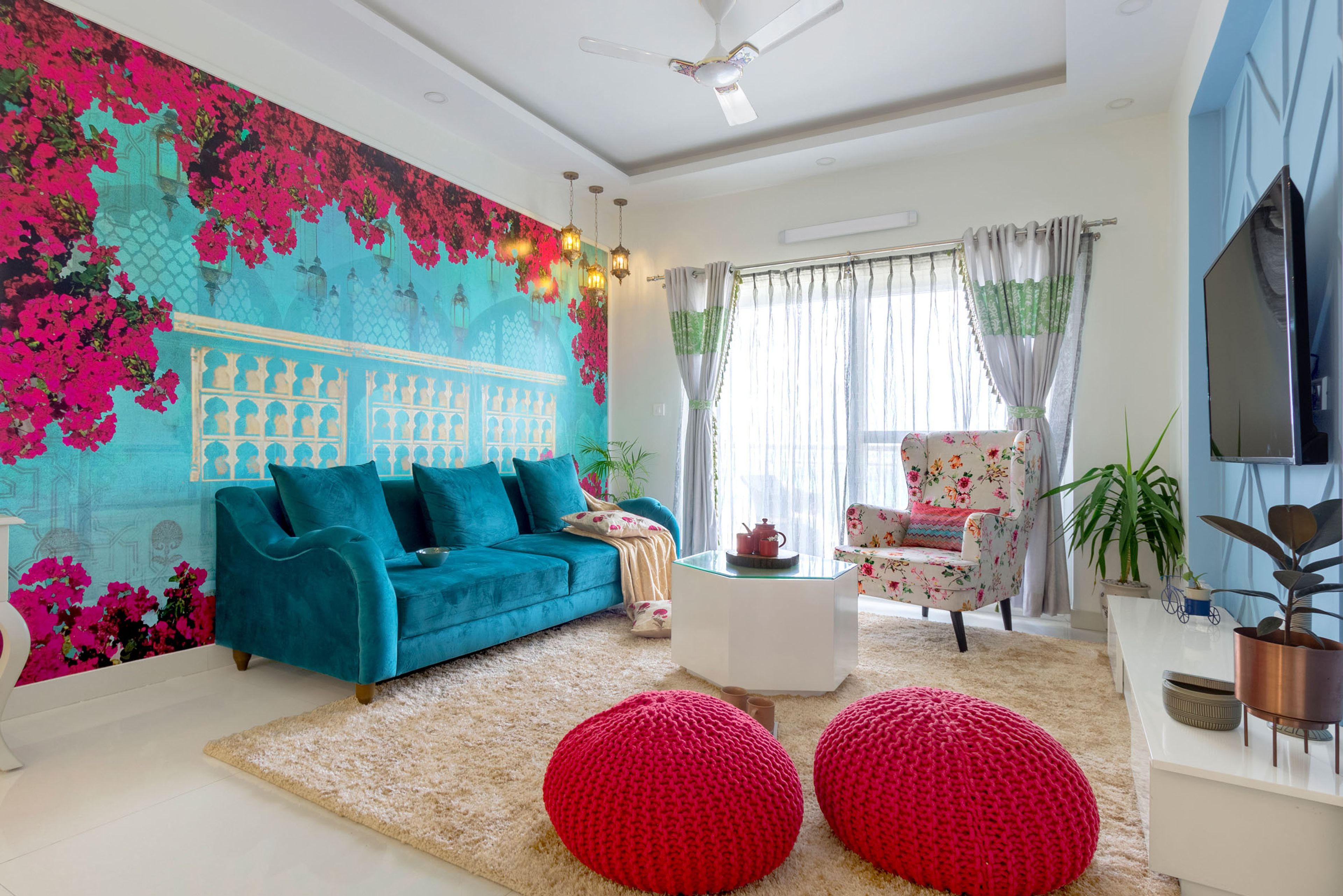 Regal Bohemian Living Room with Teal Blue Sofa, Red Pouffes, Floral Patterned Chair, and Hexagonal White Coffee Table - Livspace