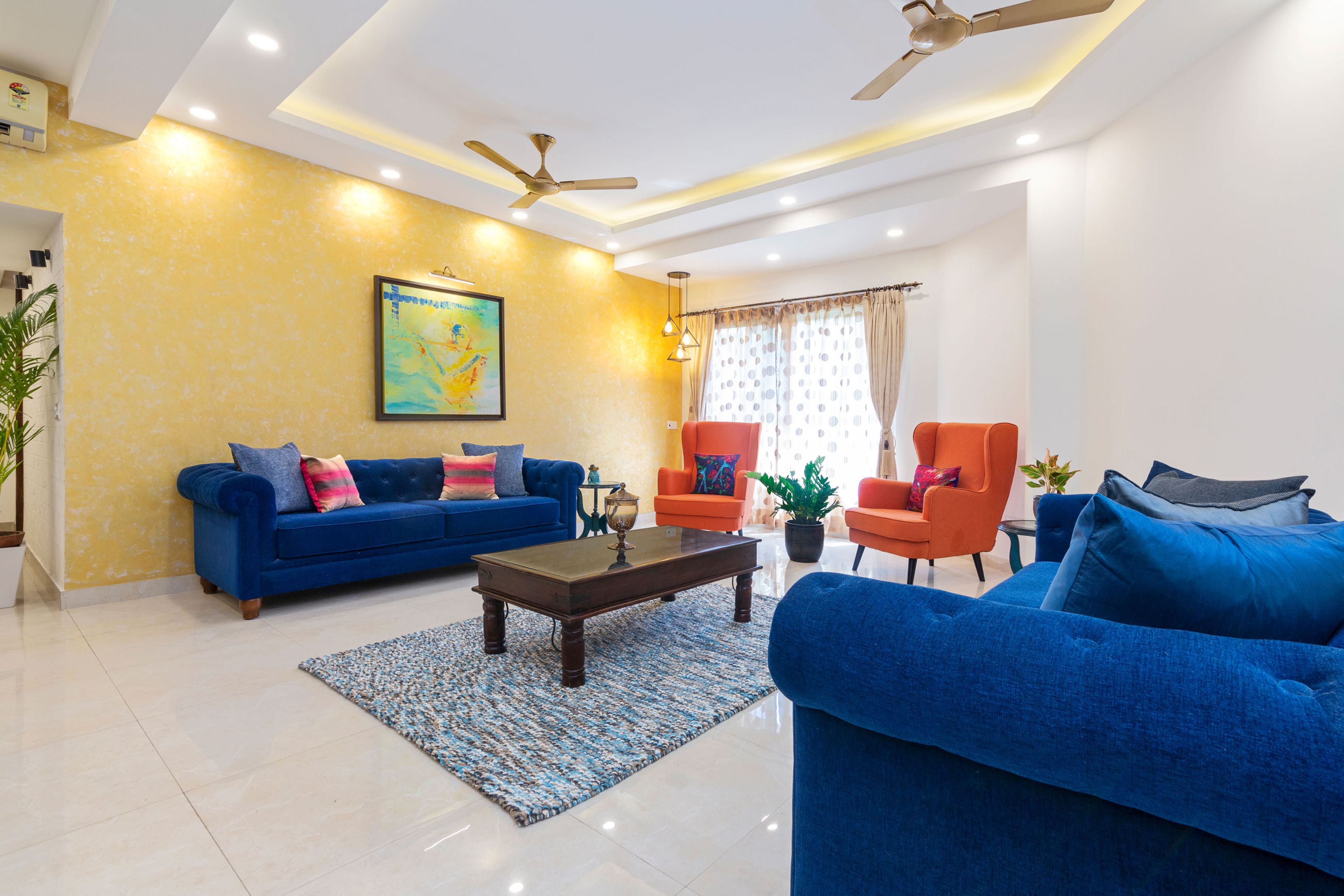 Spacious Living Room Design With Blue And Orange Upholstery With Yellow Accent Wall - Livspace