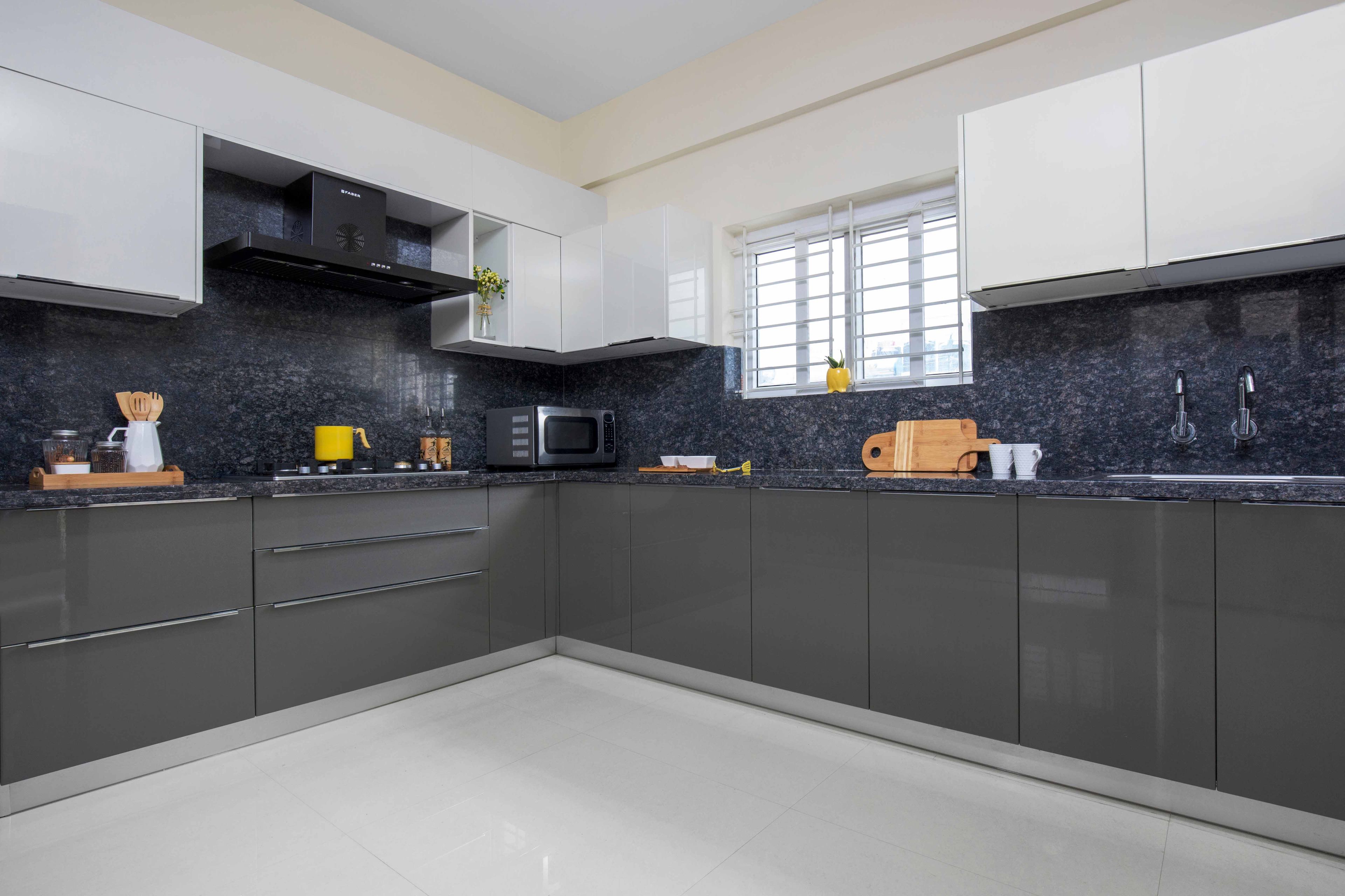 Grey and white L-shaped kitchen design with dark backsplash - Livspace