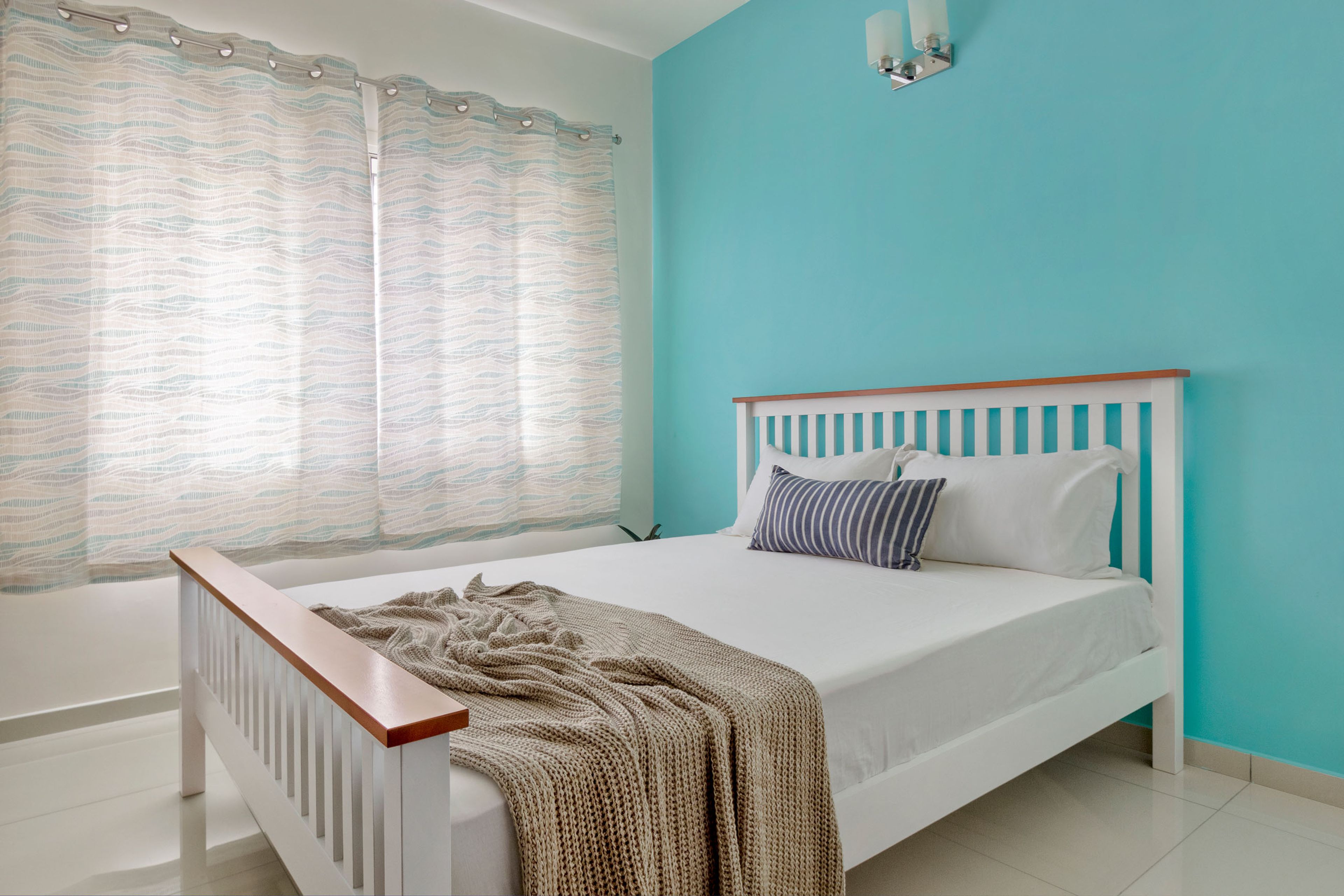 Guest room design with white bed and blue accent wall - Livspace