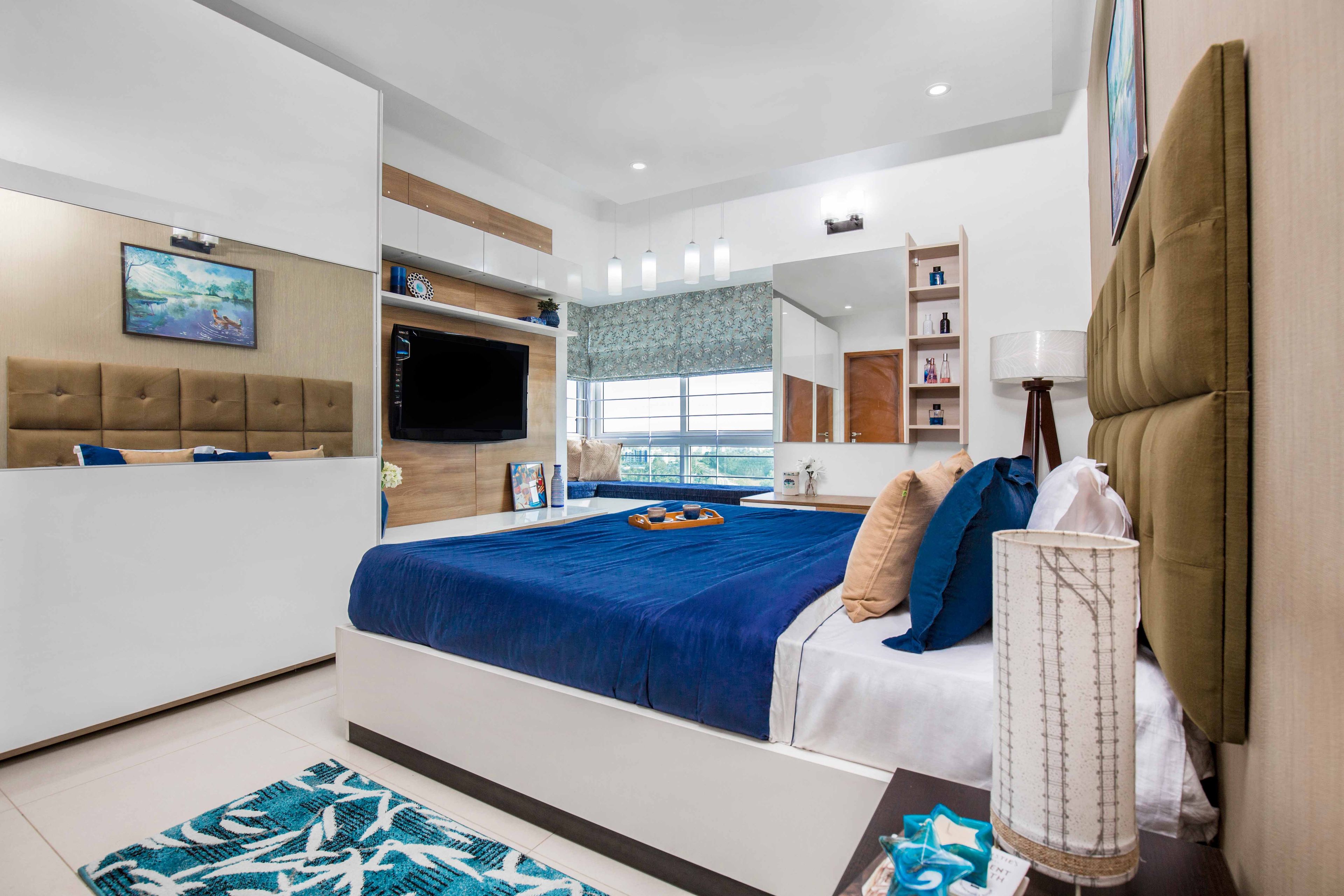 Blue and white master bedroom design with TV unit and white mirrored sliding wardrobe - Livspace