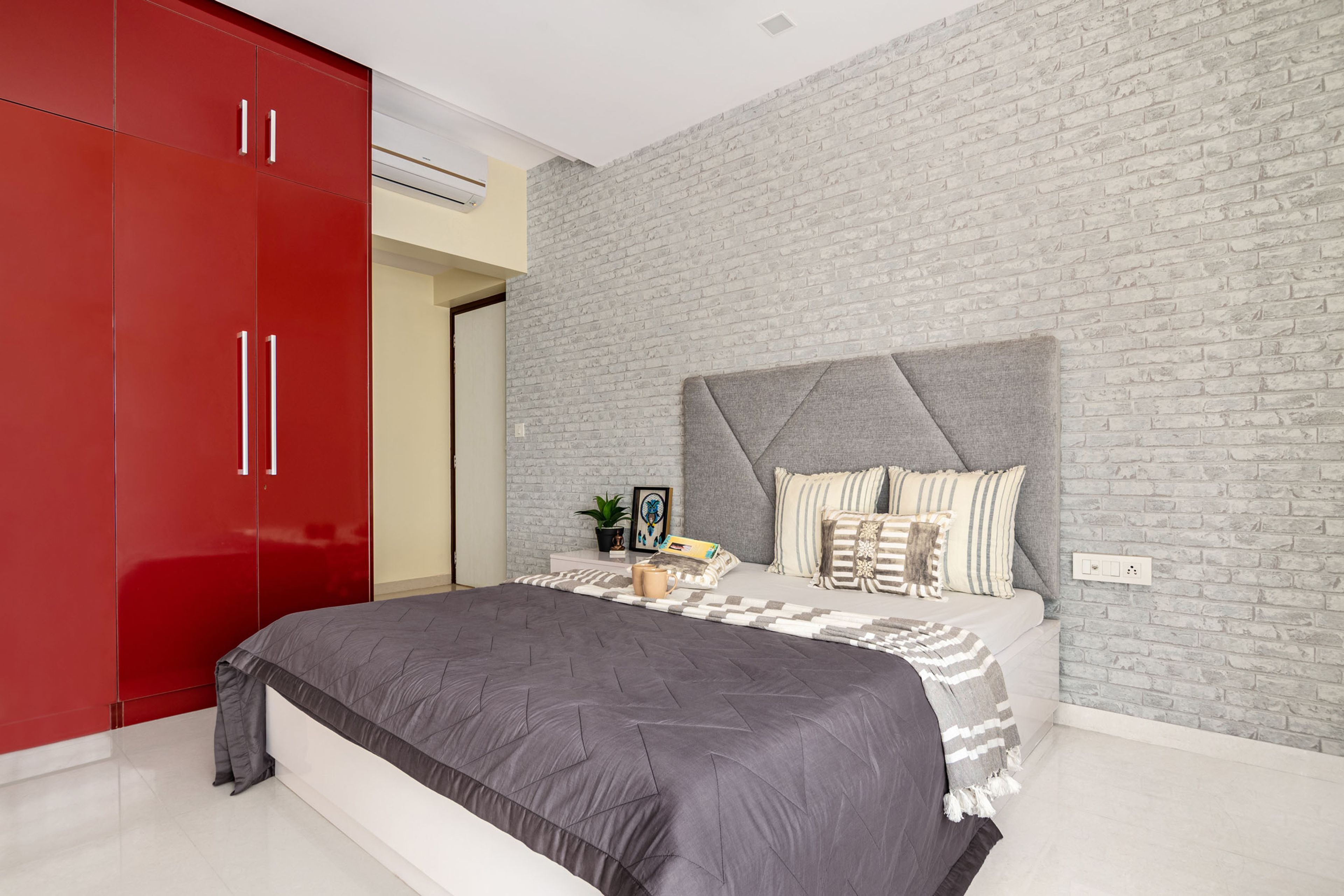 Grey master bedroom design with brick wall and red wardrobe - Livspace