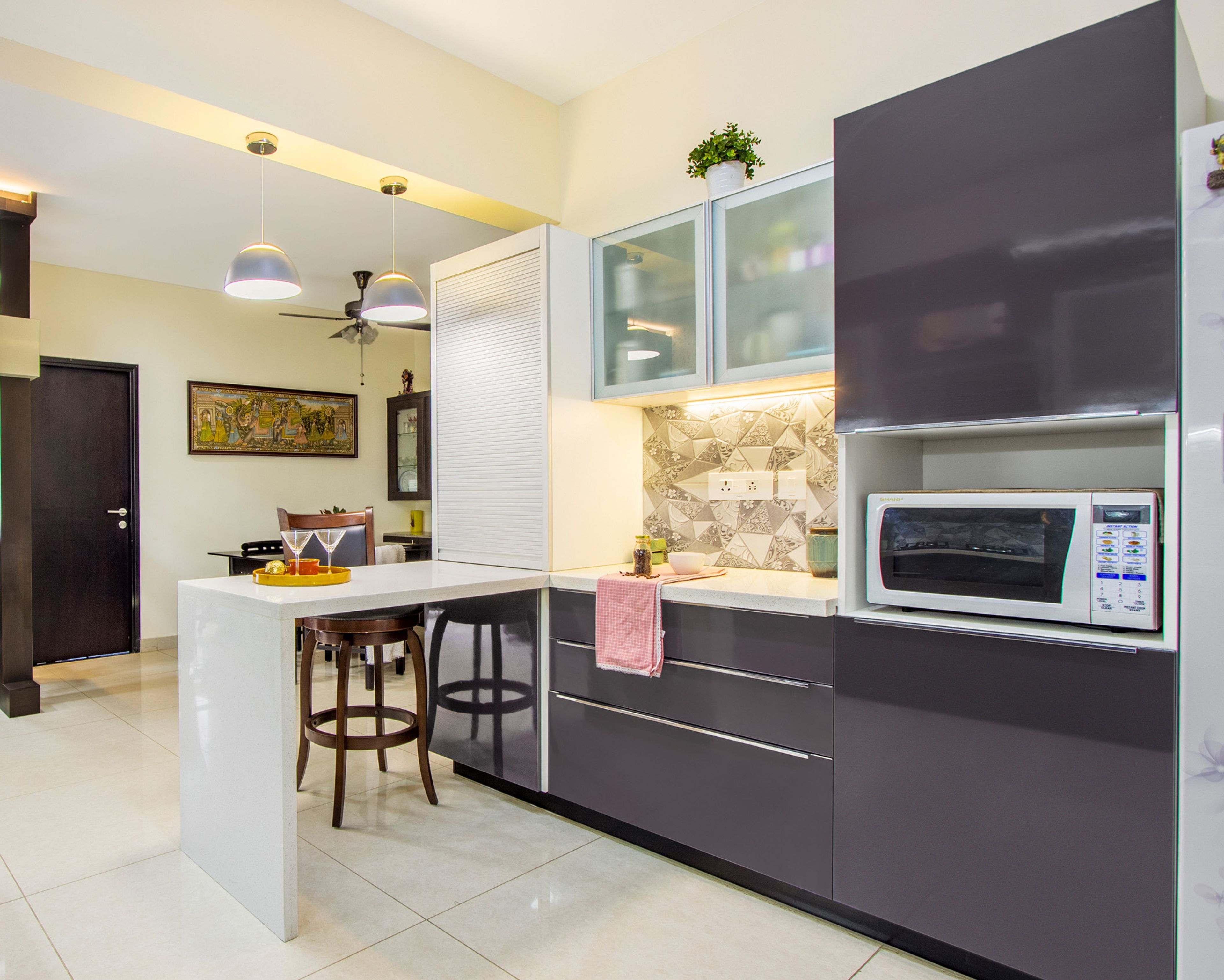 Grey and white kitchen cabinets with grey-white backsplash, aluminium rollong shutter and breakfast table - Livspace