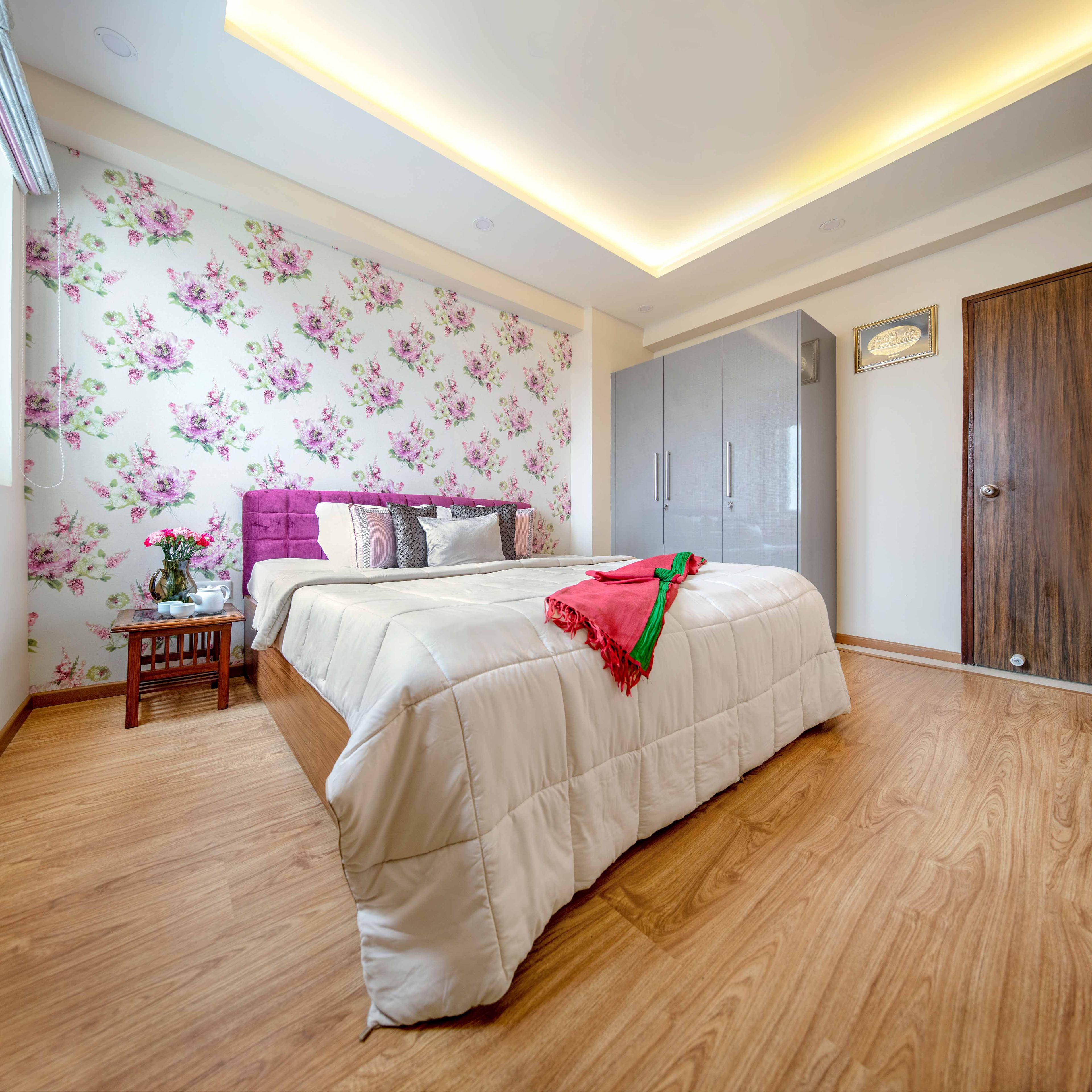Guest Bedroom With Pink Headboard, Floral Wallpaper And 3-Door Glossy Grey Wardrobe Design - Livspace