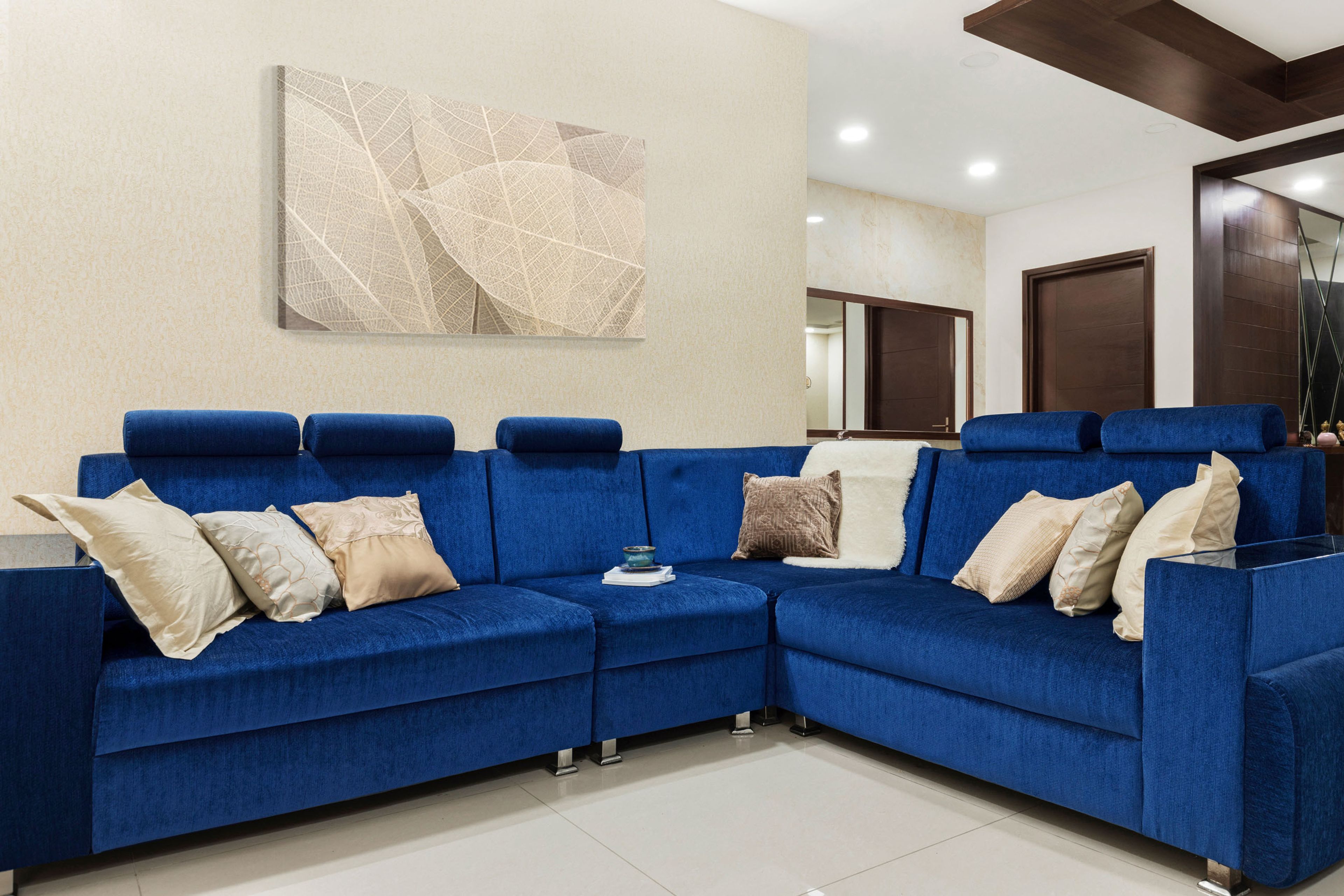 L-shaped dark blue velvet sofa set with abstract leaf wall painting - Livspace
