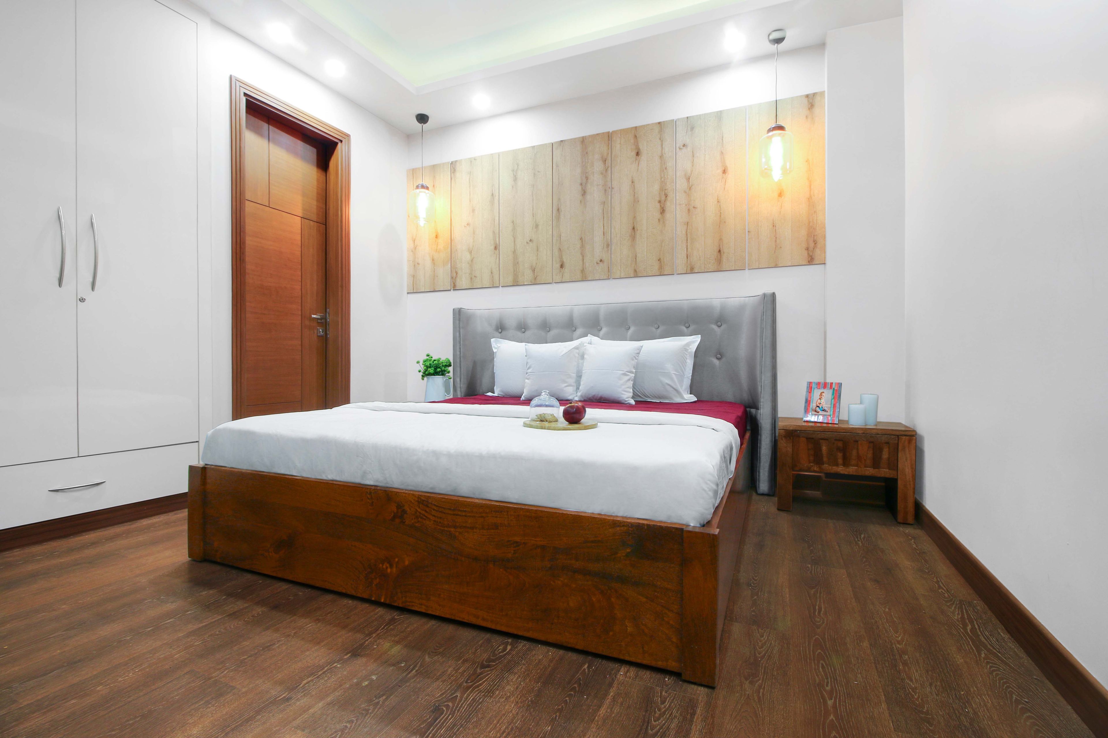 Spacious Guest Room Design With Grey Headboard, Wooden Flooring And White Swing Wardrobe - Livspace