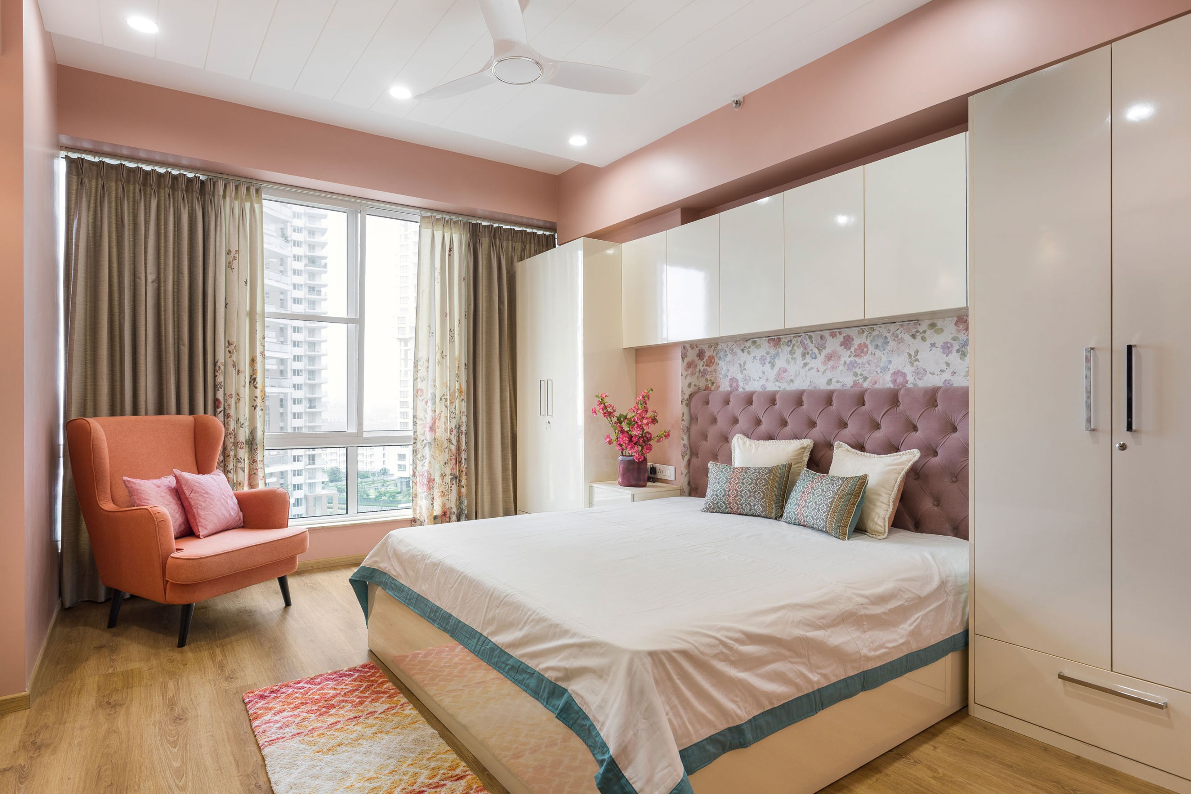 Guest Room With Pink Tufted Headboard, Floral Wallpaper And 4-Door White Swing Wardrobe WIth Loft Storage - Livspace