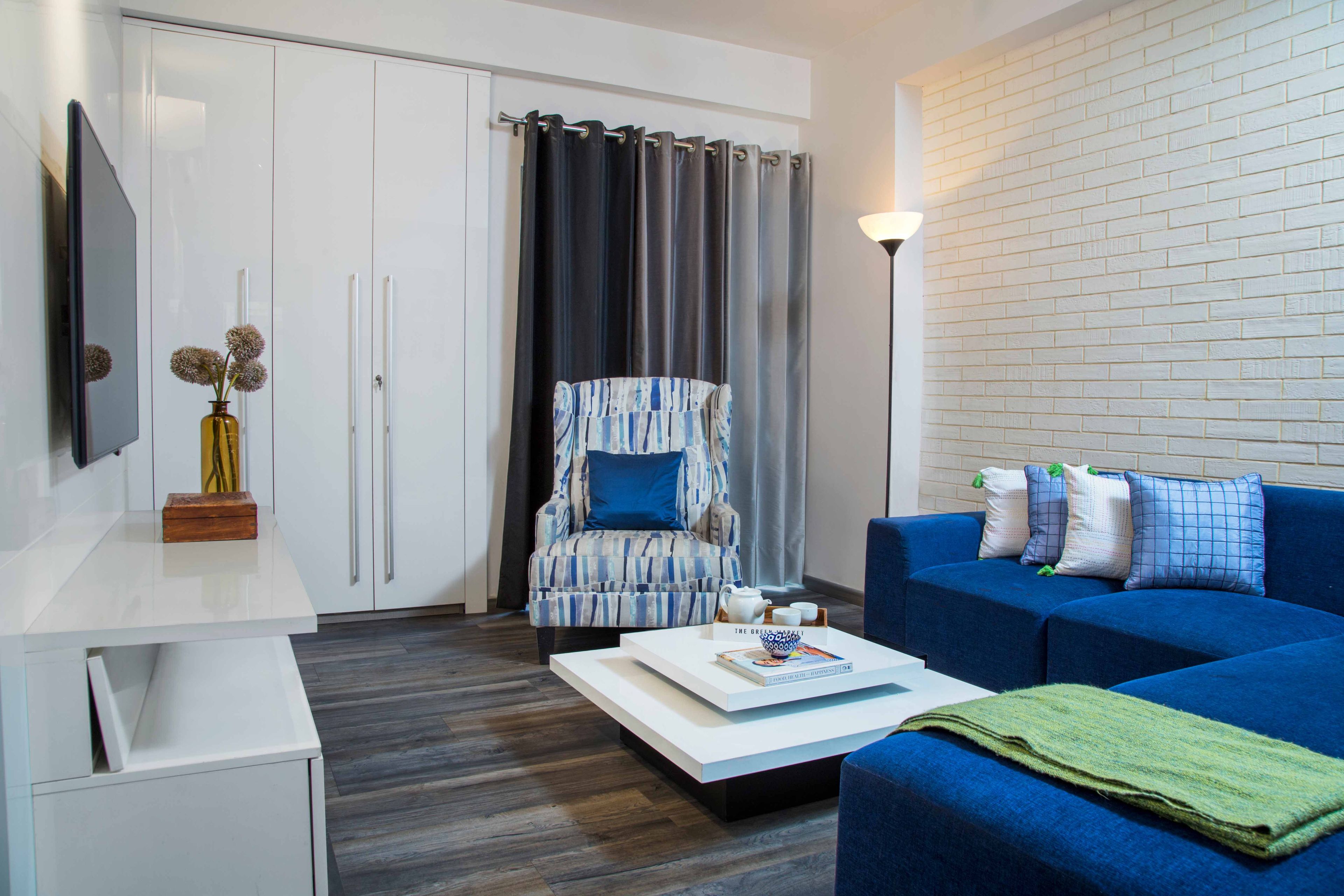 Family Room With Blue Sectional, White TV Unit And White 3-Door Swing Wardrobe - Livspace