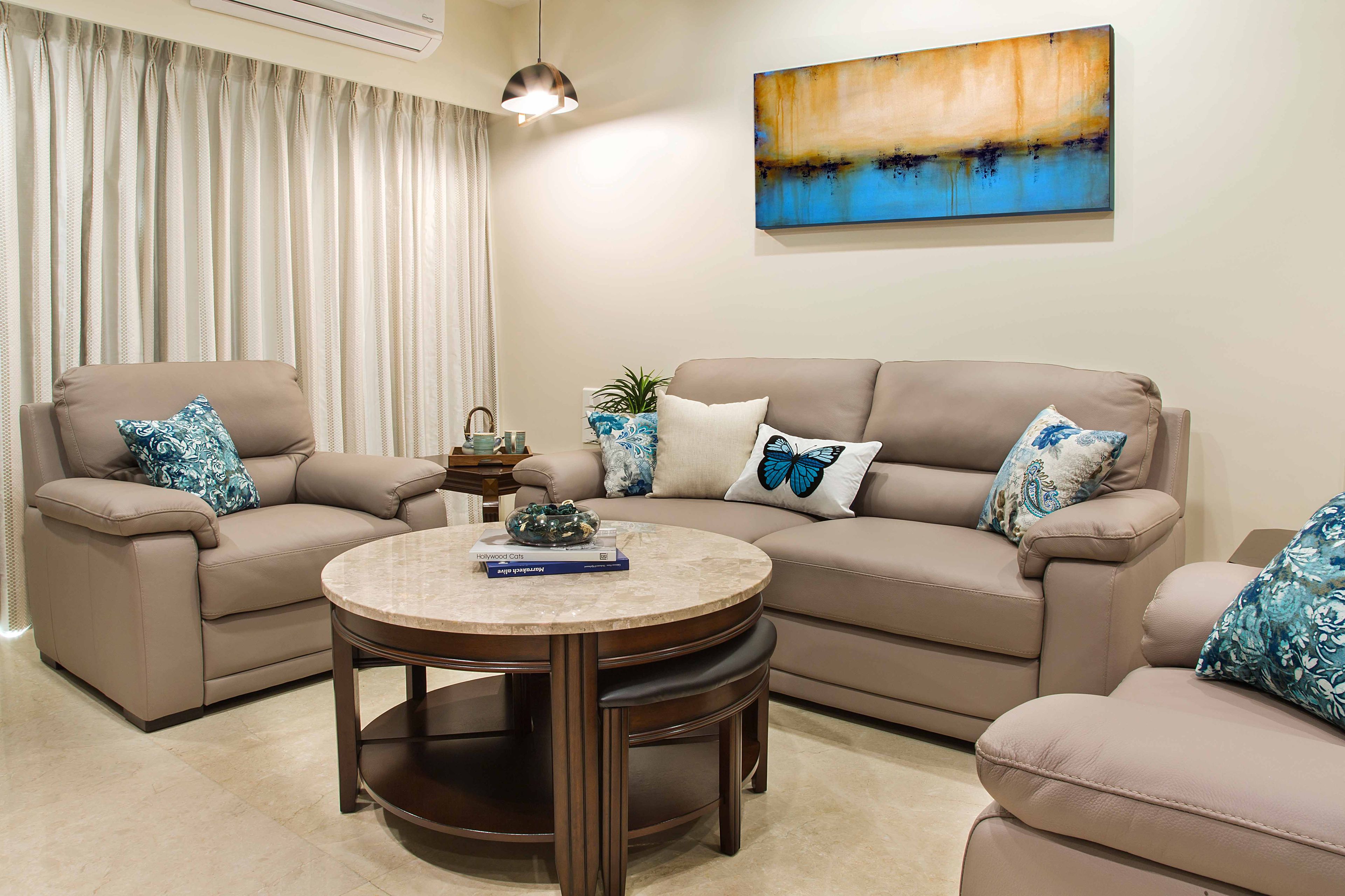 U-Shaped Beige Leather Sofa Set With With Blue Patterned Cushions And Round Off-White Coffee Table - Livspace