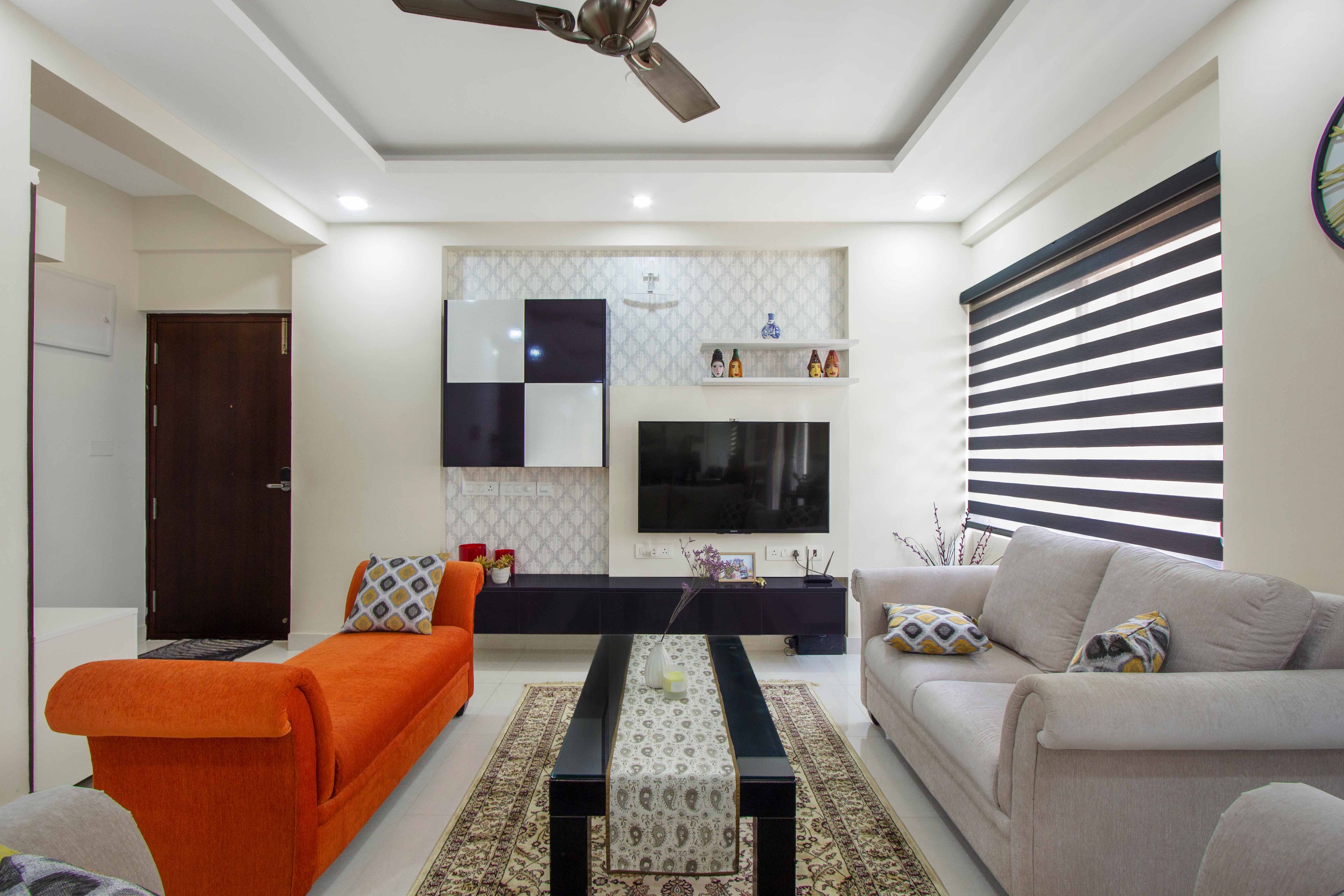 Living Room Design with Grey 3-Seater Sofa, Orange Seating Bench, and Black and White TV Unit - Livspace