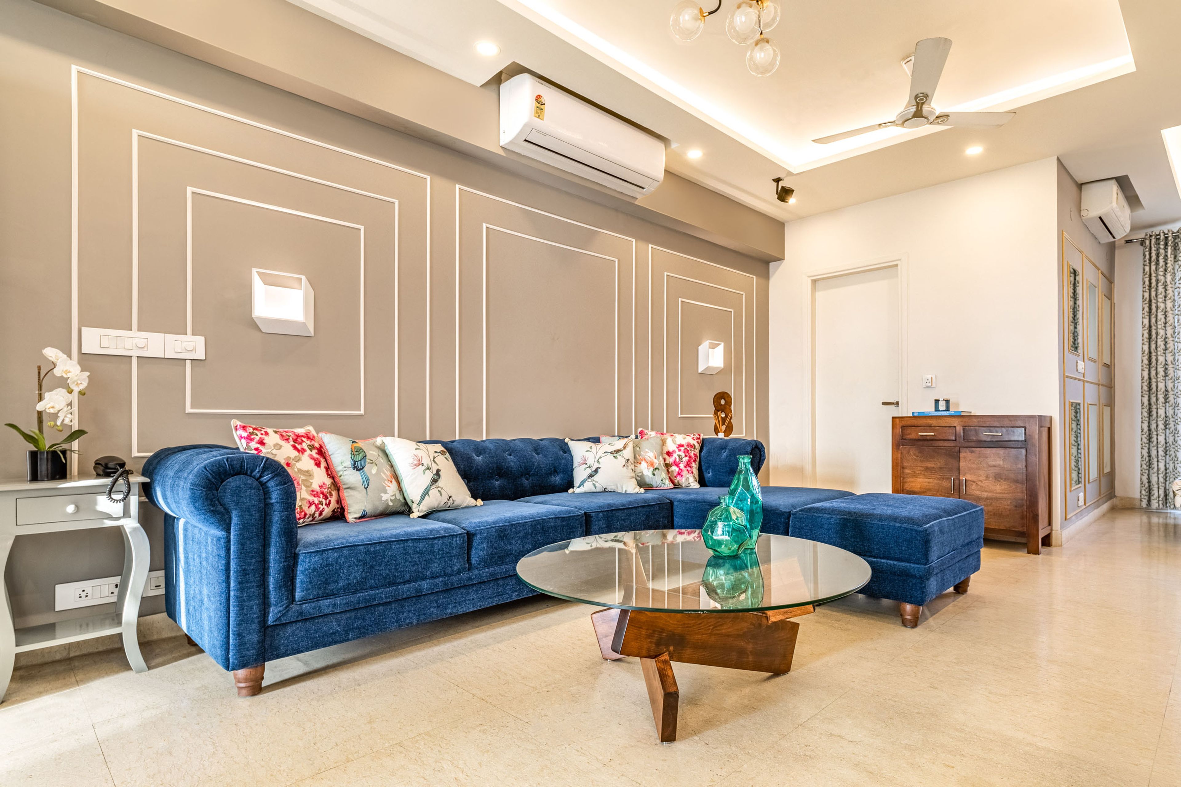 Spacious Living Room With Blue Velvet Sectional And Beige Wall With White Trims- Livspace