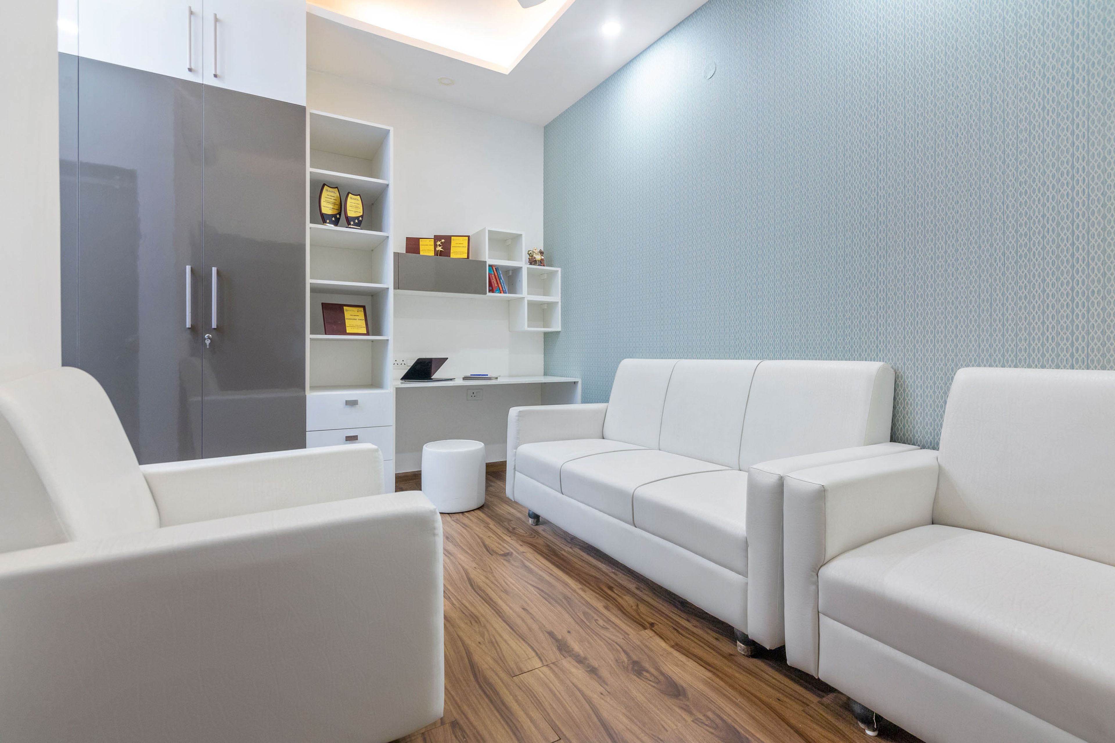 Spacious White Home Office WIth Pristine White Sofa Set, Light Blue Wallpaper, Study Table And 2-Door Grey And White Glossy Swing Wardrobe - Livspace