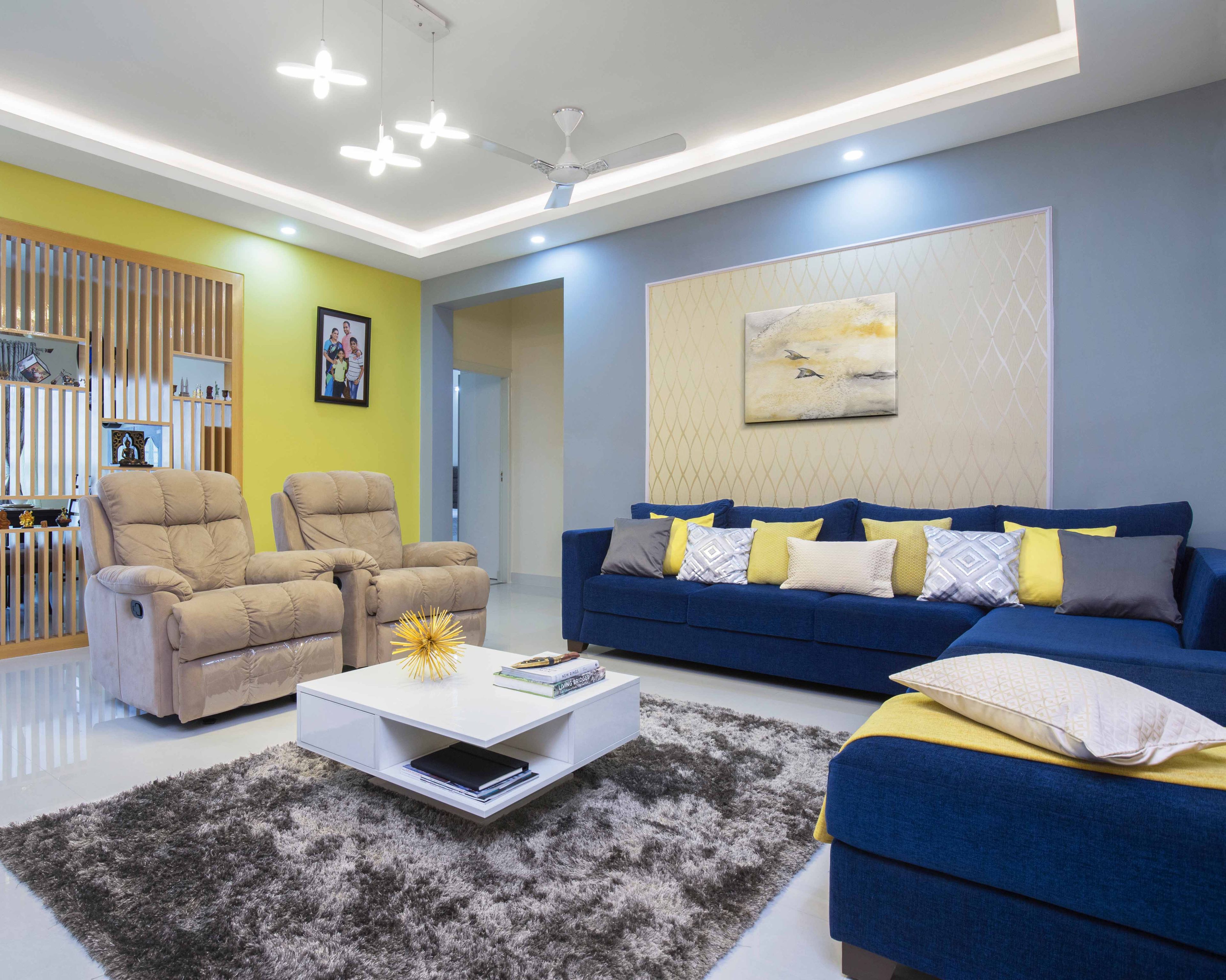 Living Room Design With Dark Blue L-Shaped Sectional, White Square Coffee Table, Two Beige Accent Chairs And Blue-Yellow Accent Walls - Livspace