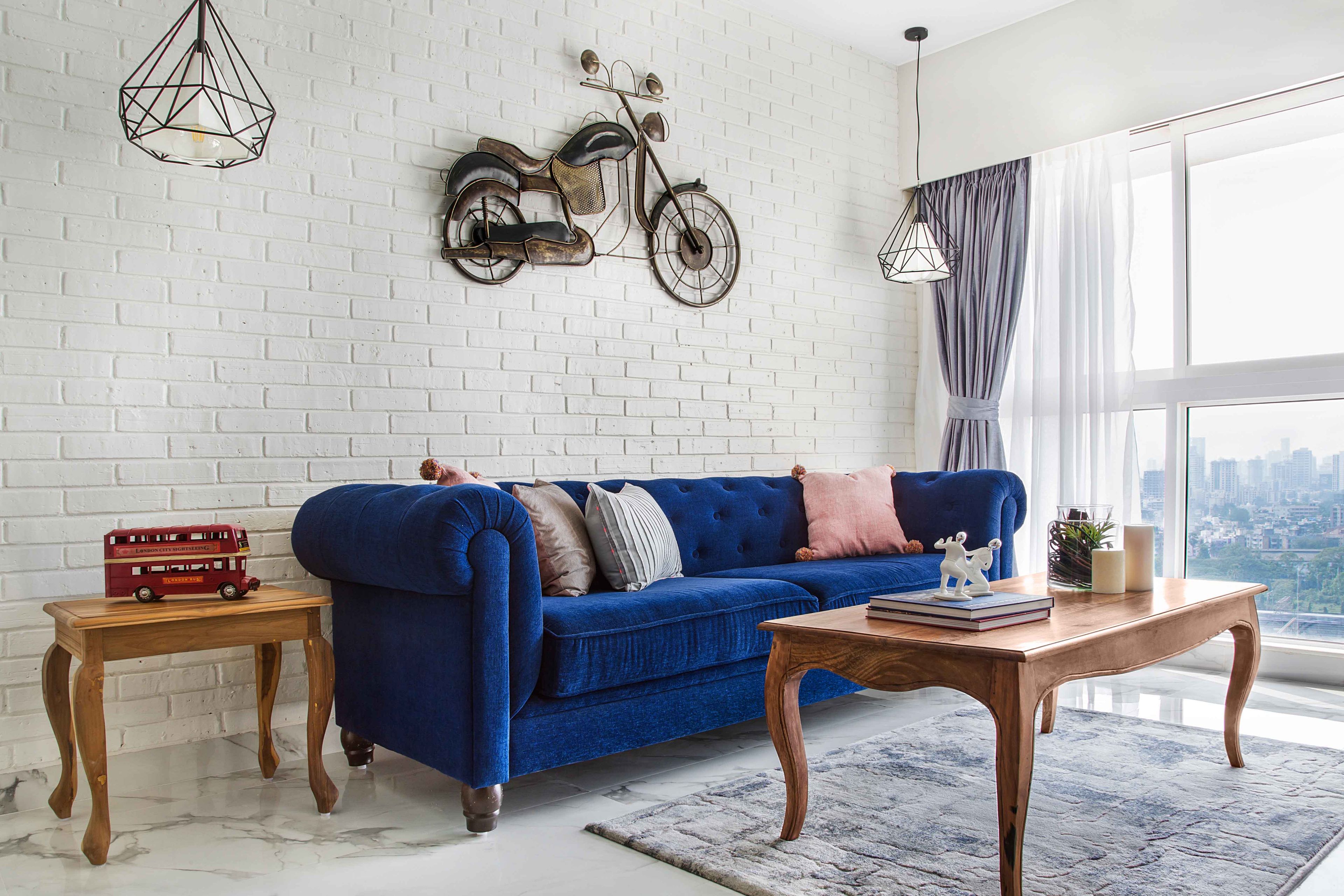 Spacious Living Room Design With Dark Blue Chesterfield Sofa, Wooden Side Tables And White Brick Accent Wall - Livspace