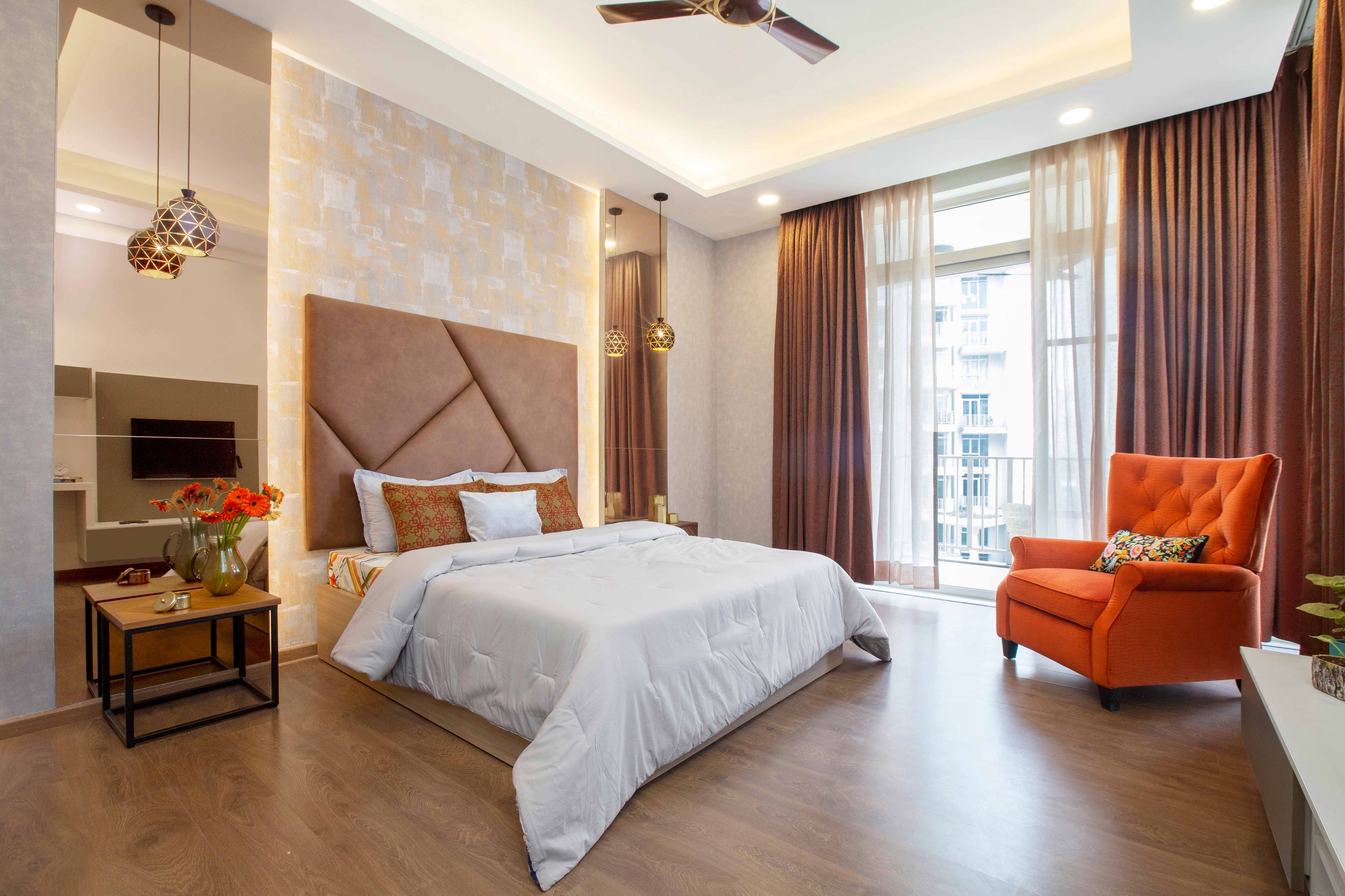 Master Bedroom Design With Brown Panelled Headboard, Orange Accent Chair, Beige Patterned Wallpaper, Hanging Lights And Floor-To-Ceiling Mirror Panels - Livspace