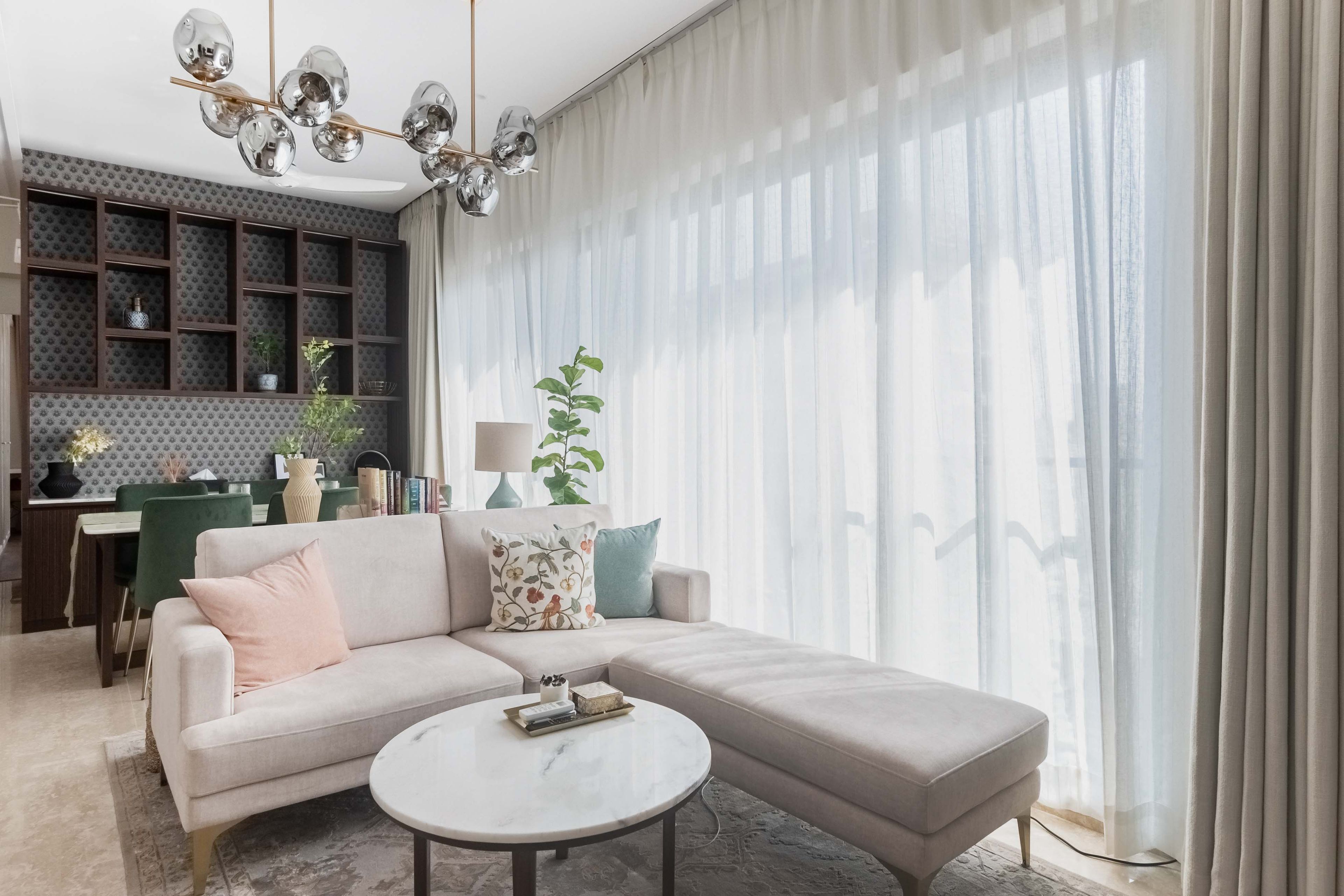 Beige sofa and ottoman with chandelier and open wall units - Livspace