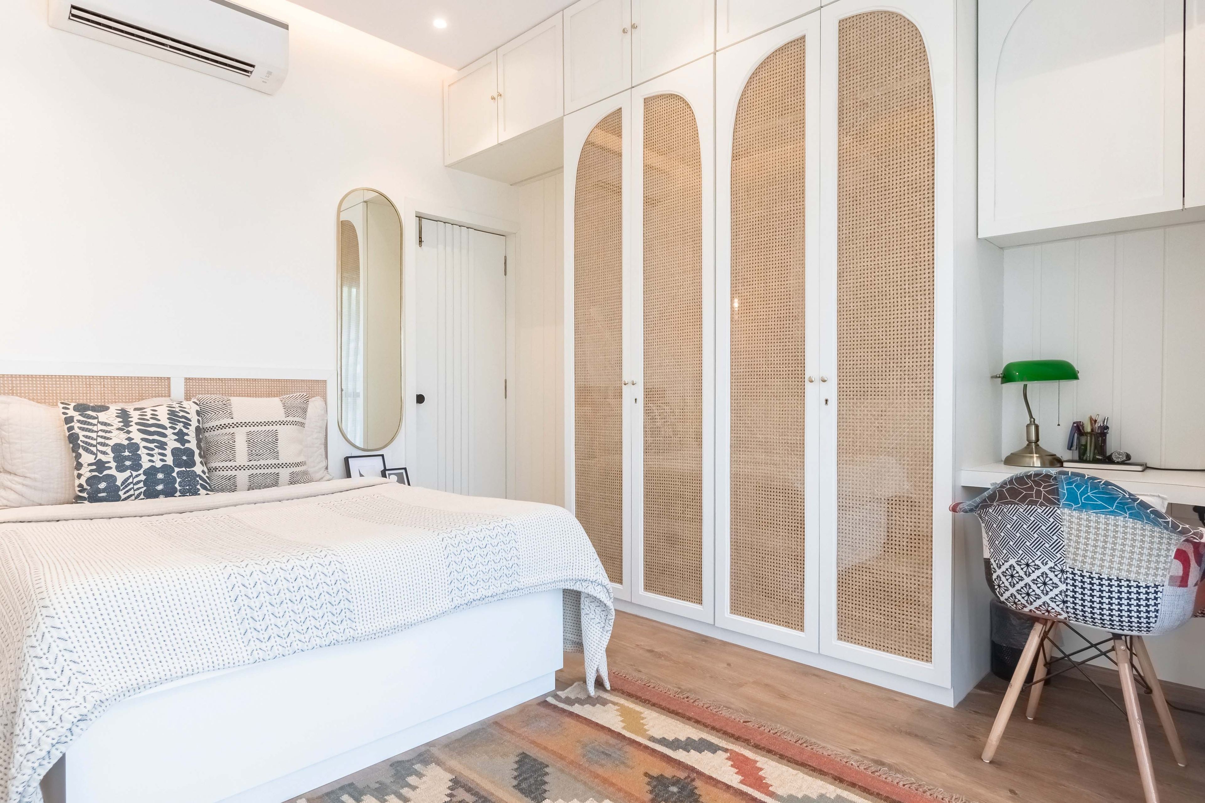 Master bedroom with 4-door swing wardrobe with loft in white and rattan finish and a work table - Livspace