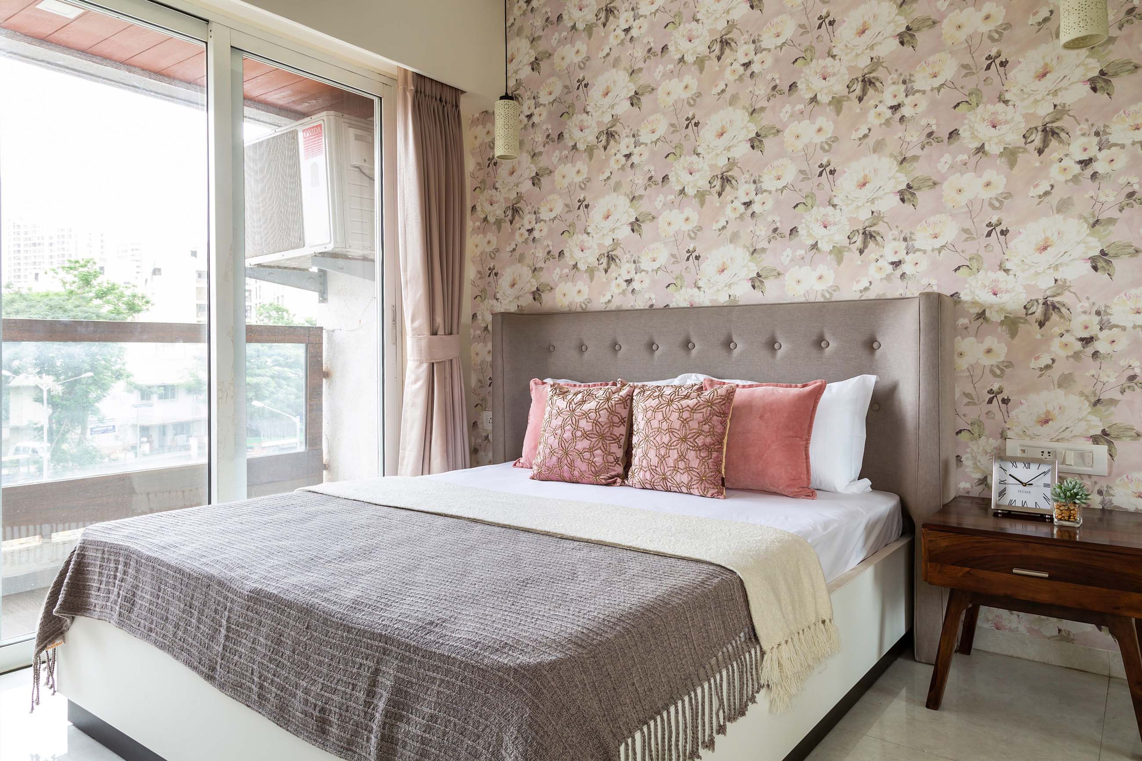 Master bedroom with floral wallpaper and grey tufted headboard - Livspace