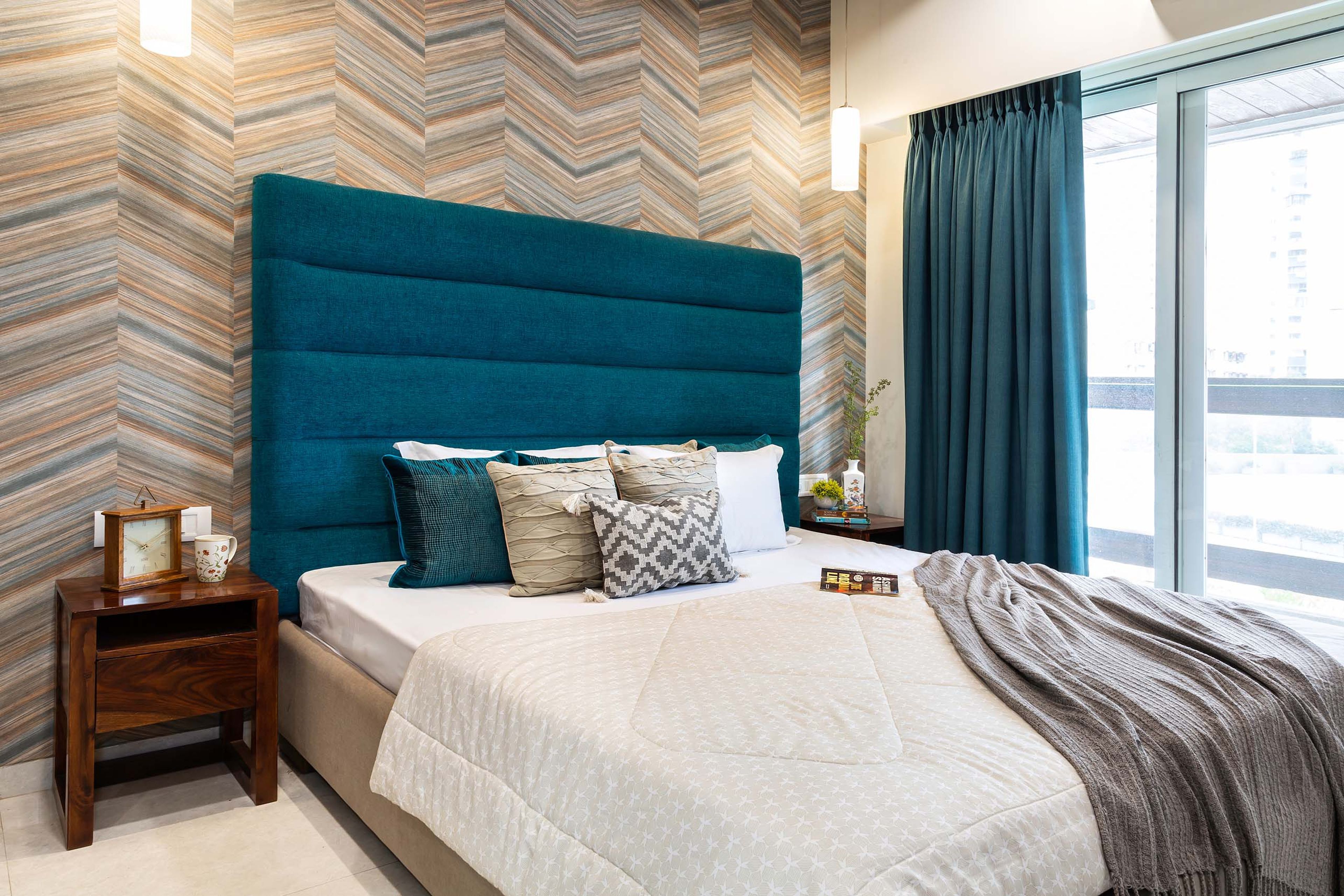 Guest bedroom with abstract wallpaper and blue tufted headboard - Livspace