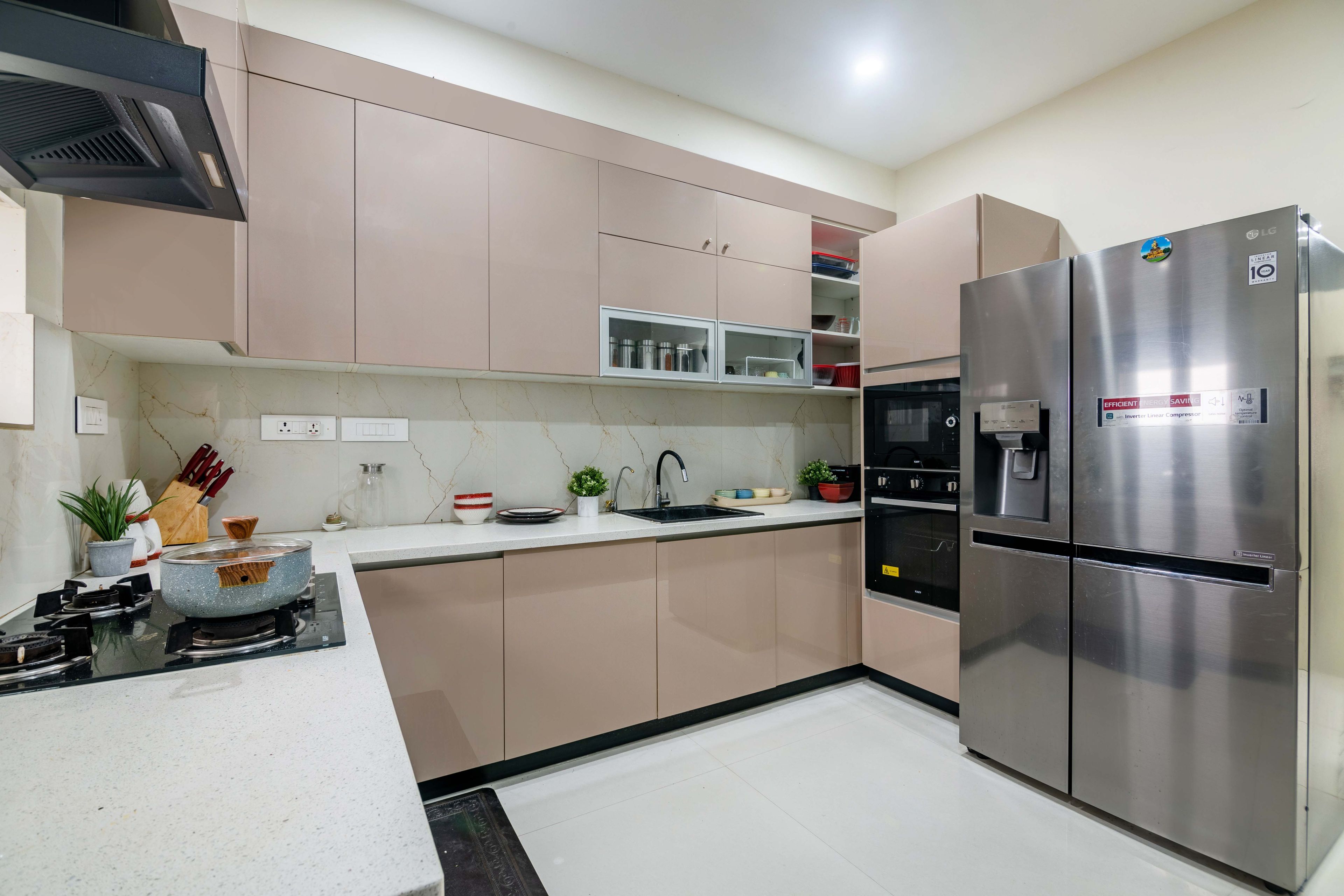 L shape beige kitchen with marble backsplash and kitchen appliances - Livspace
