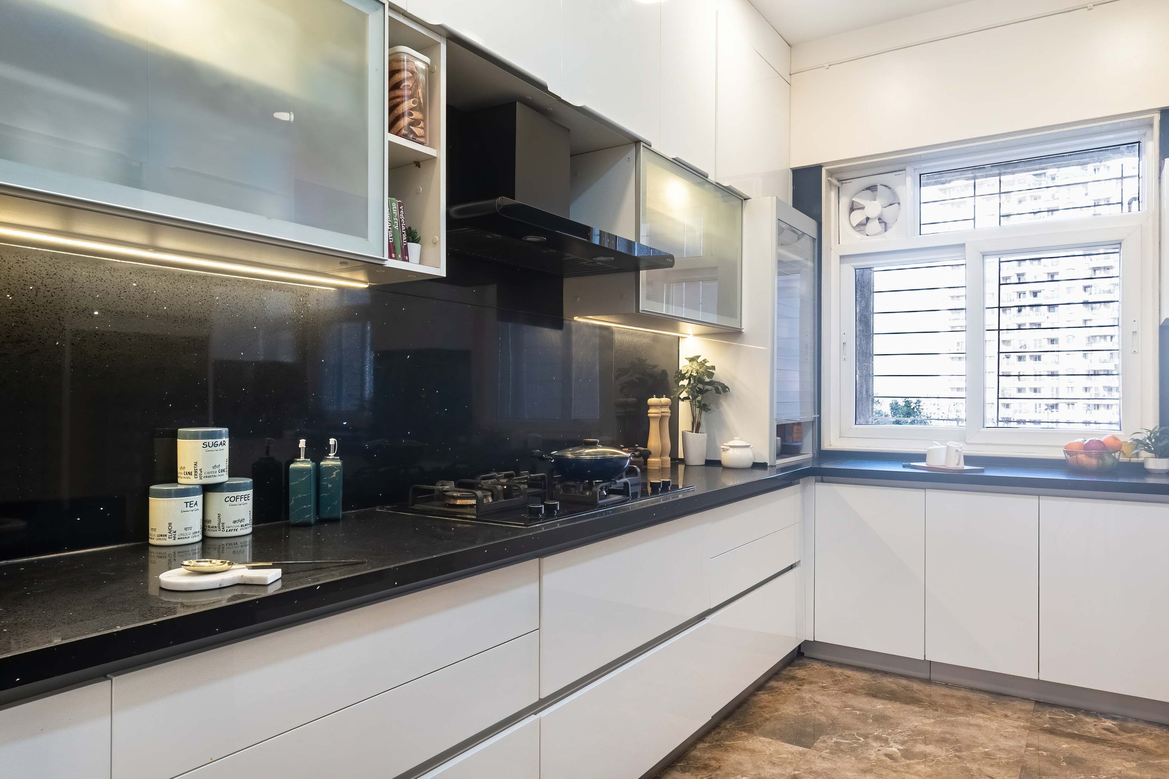 L shaped white kitchen design with black countertop and dado tiles - Livspace