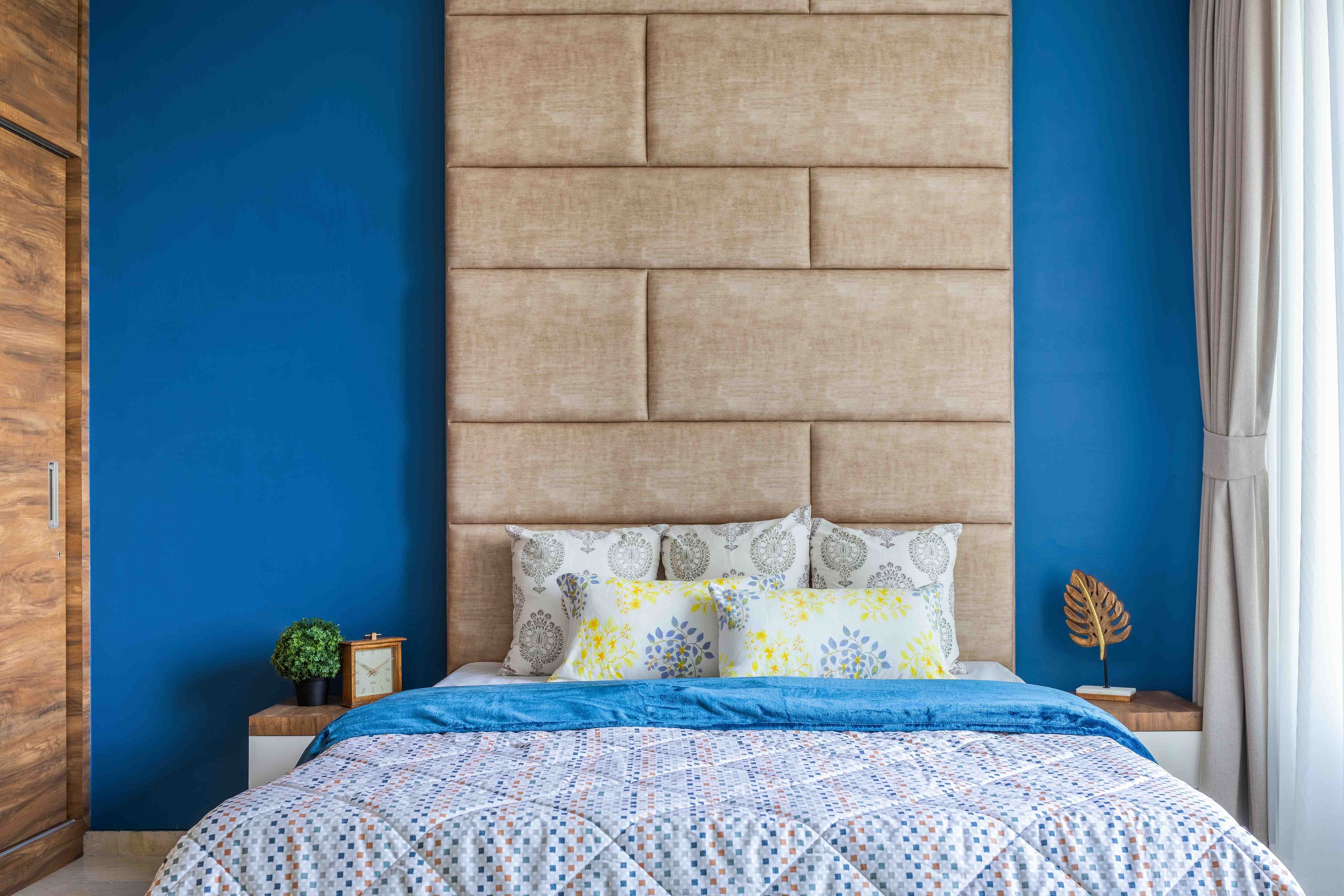 Blue bedroom with beige tufted headboard and bedside stands - Livspace