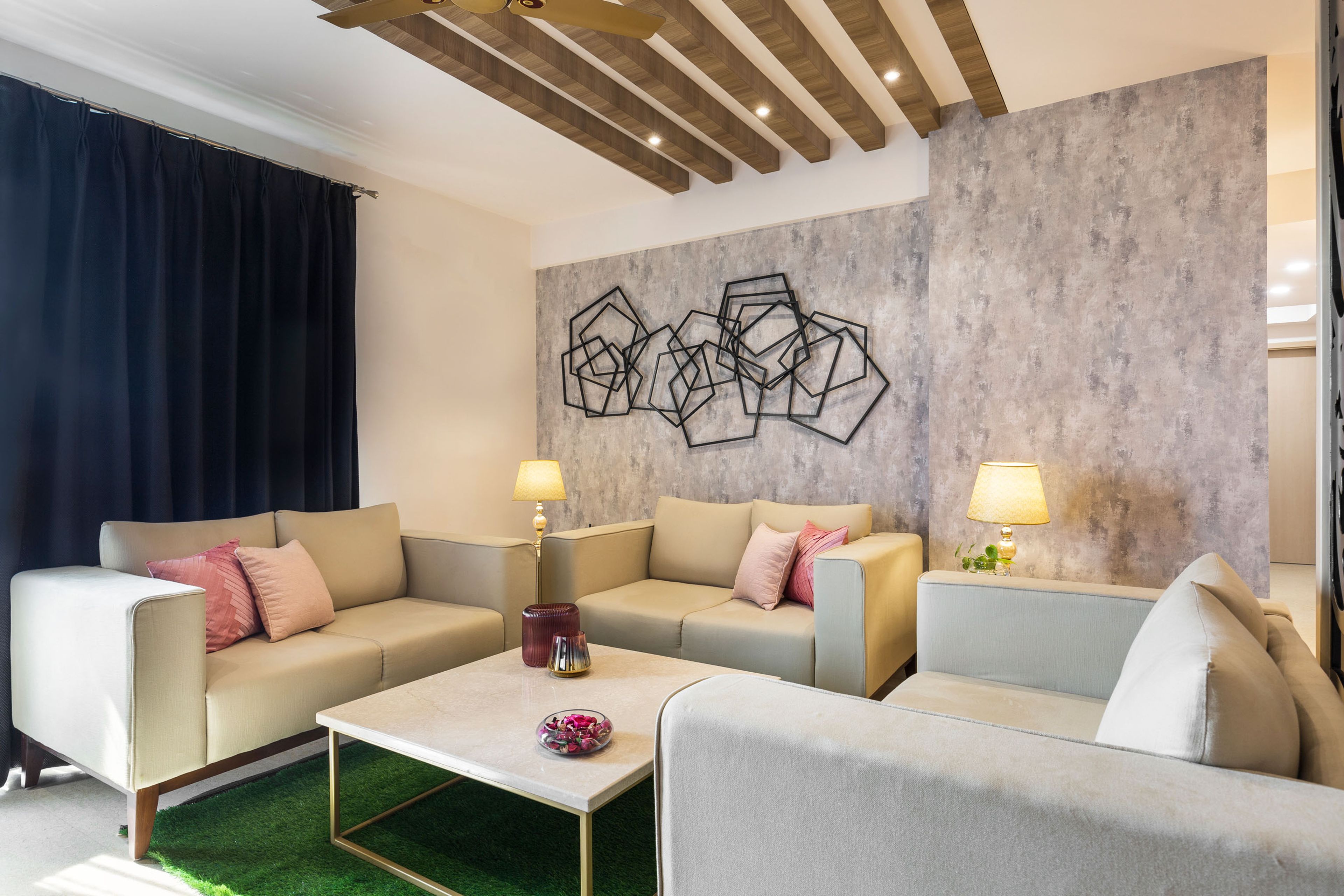 Spacious living room with U-shaped cream toned sofas and textured grey wall - Livspace