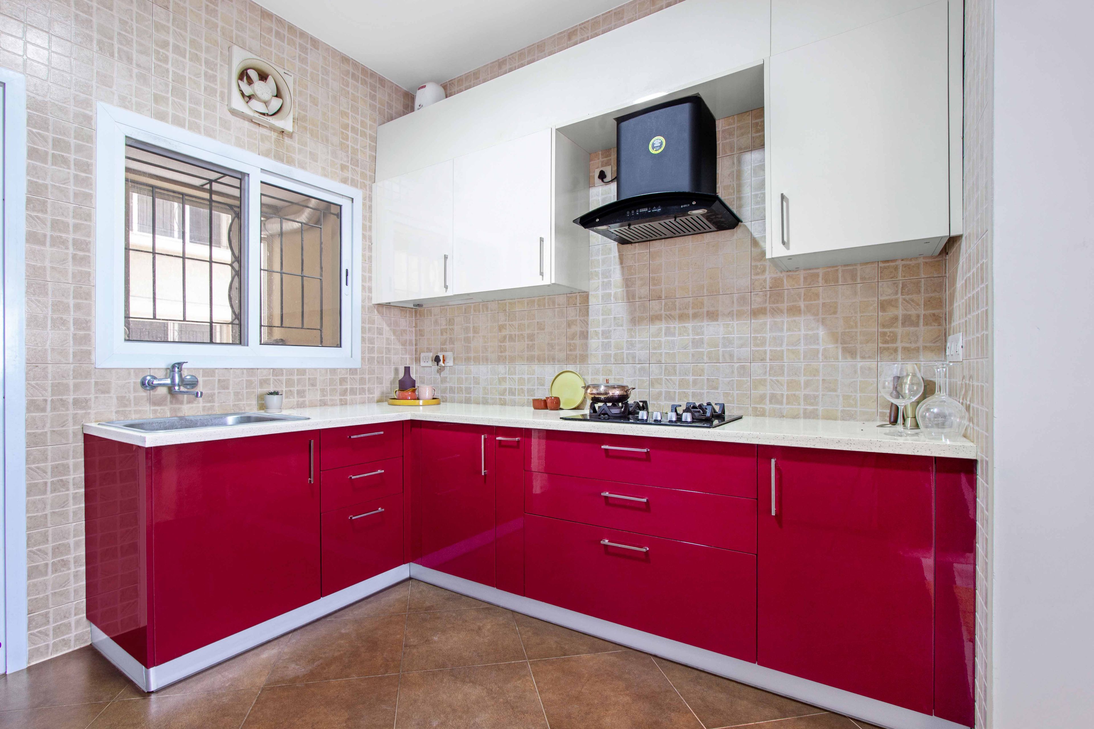 L shaped red and white kitchen with beige wall tiles - Livspace