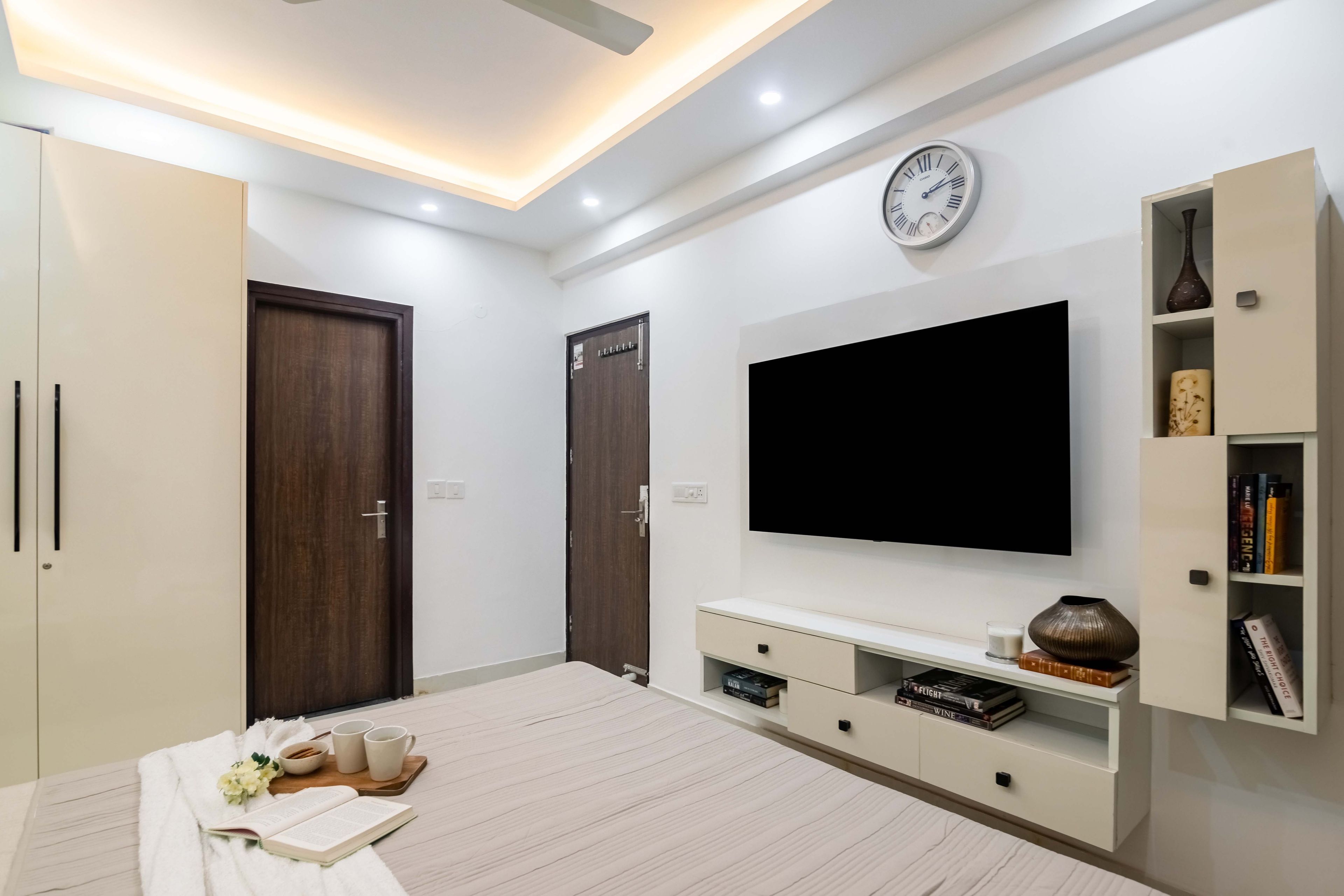 White wall-mounted TV unit design for the master bedroom, with open and closed storage unit - Livspace
