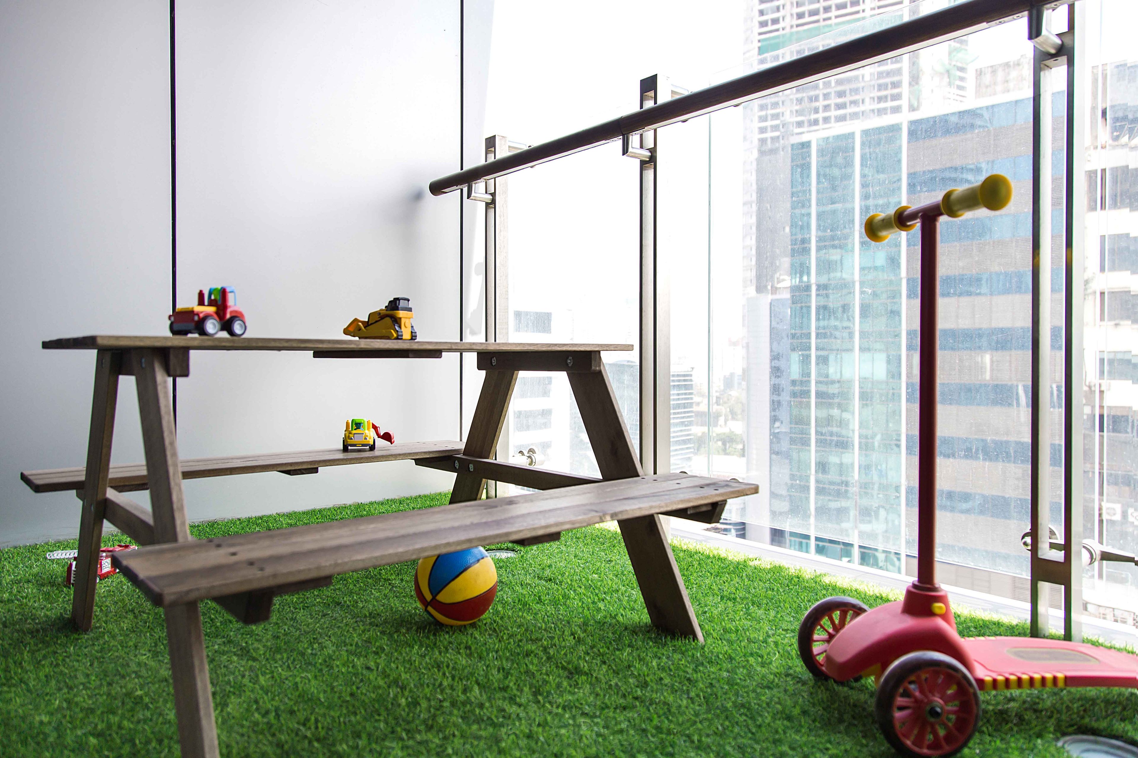 Spacious balcony with wooden table, bench and green grass mat- Livspace