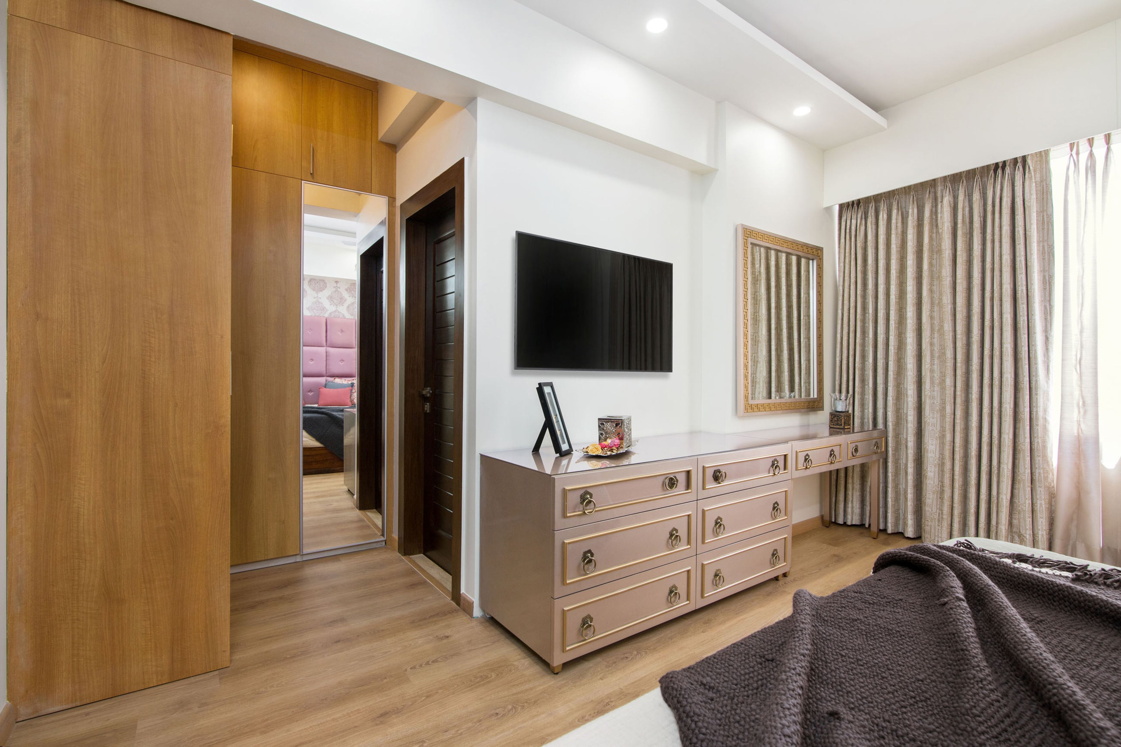 Floor-mounted light pink TV console with drawer storage and wooden walk in wardrobe for guest room - Livspace