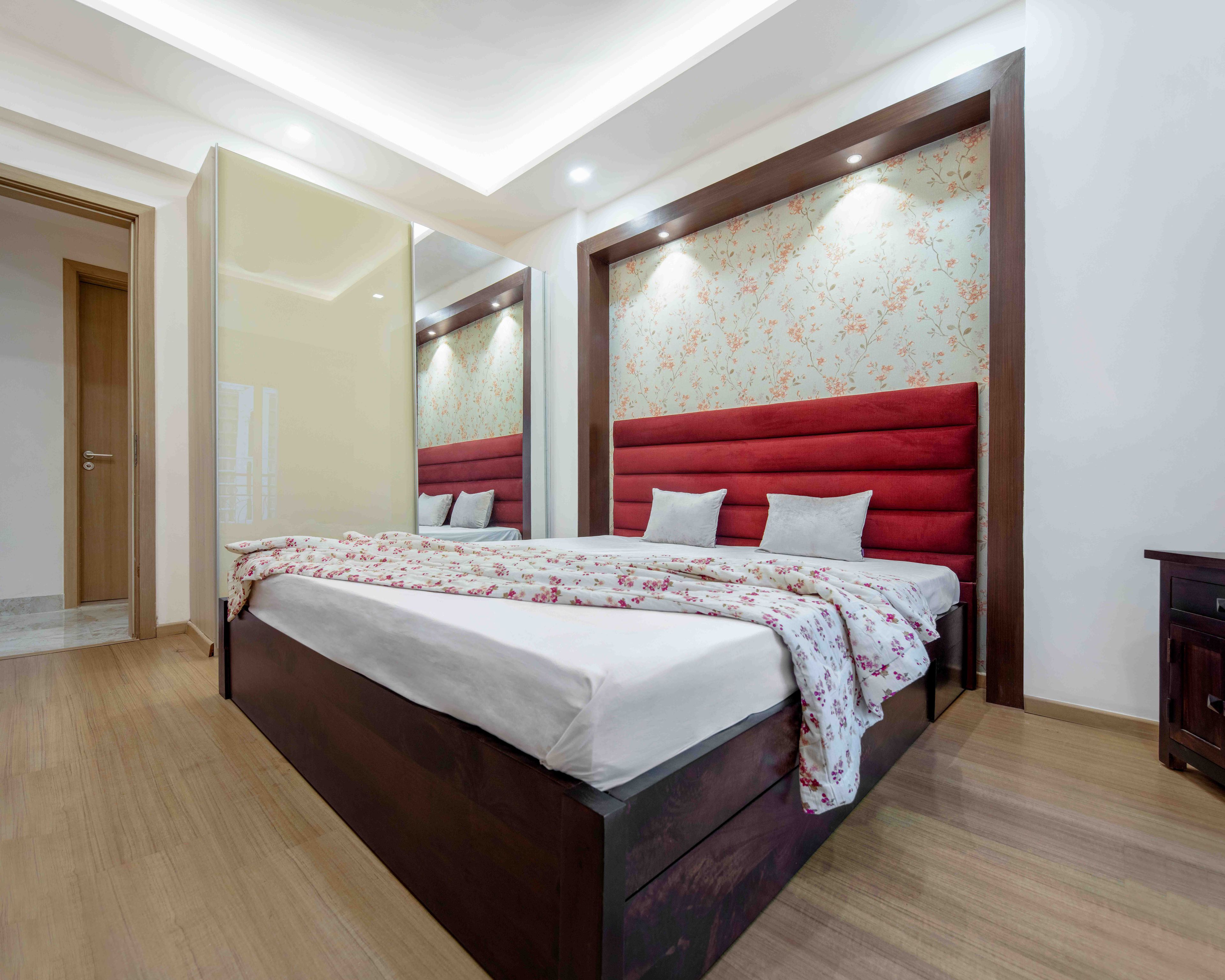 Second guest room with queen sized bed, red headboard and beige sliding wardrobe - Livspace