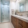 Dual vanity bathroom with glass shower, wooden cabinetry, and expansive wall mirror