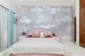 Pastel kids’ bedroom with cloud mural, pink headboard, light blue curtains, and cozy bedding